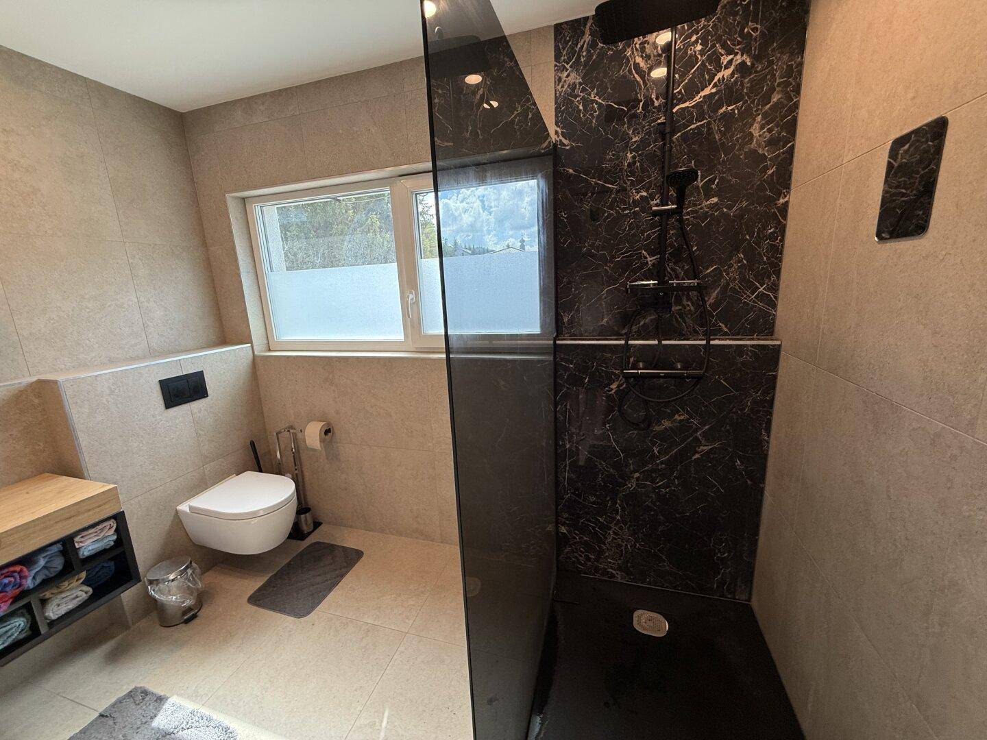 Modernes Badezimmer mit begehbarer Dusche, Wand-WC und großformatigen Fliesen an Wänden und Boden.