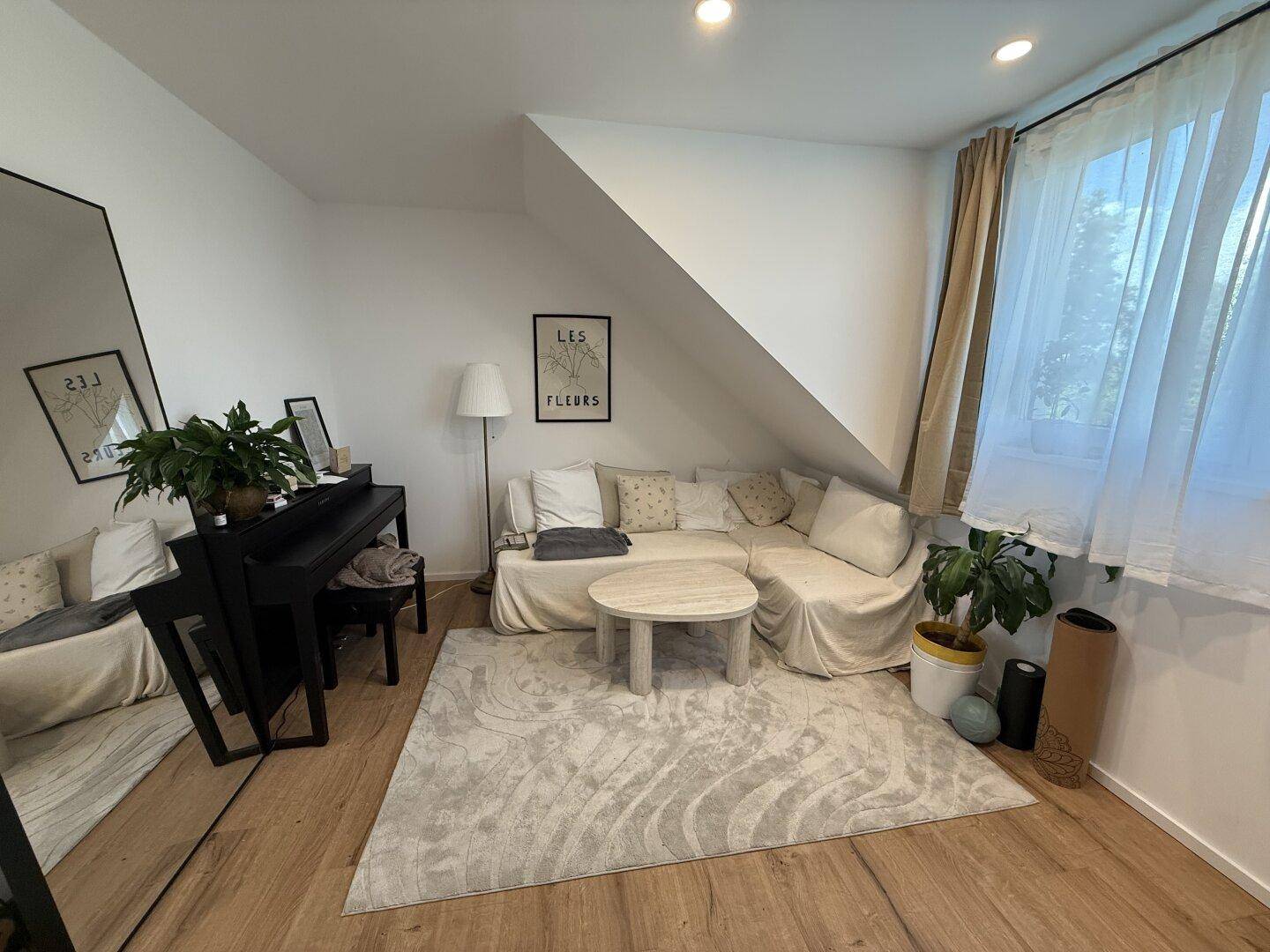 Gemütliches Wohnzimmer im Dachgeschoss mit Dachschrägen, Holzboden und viel Tageslicht.