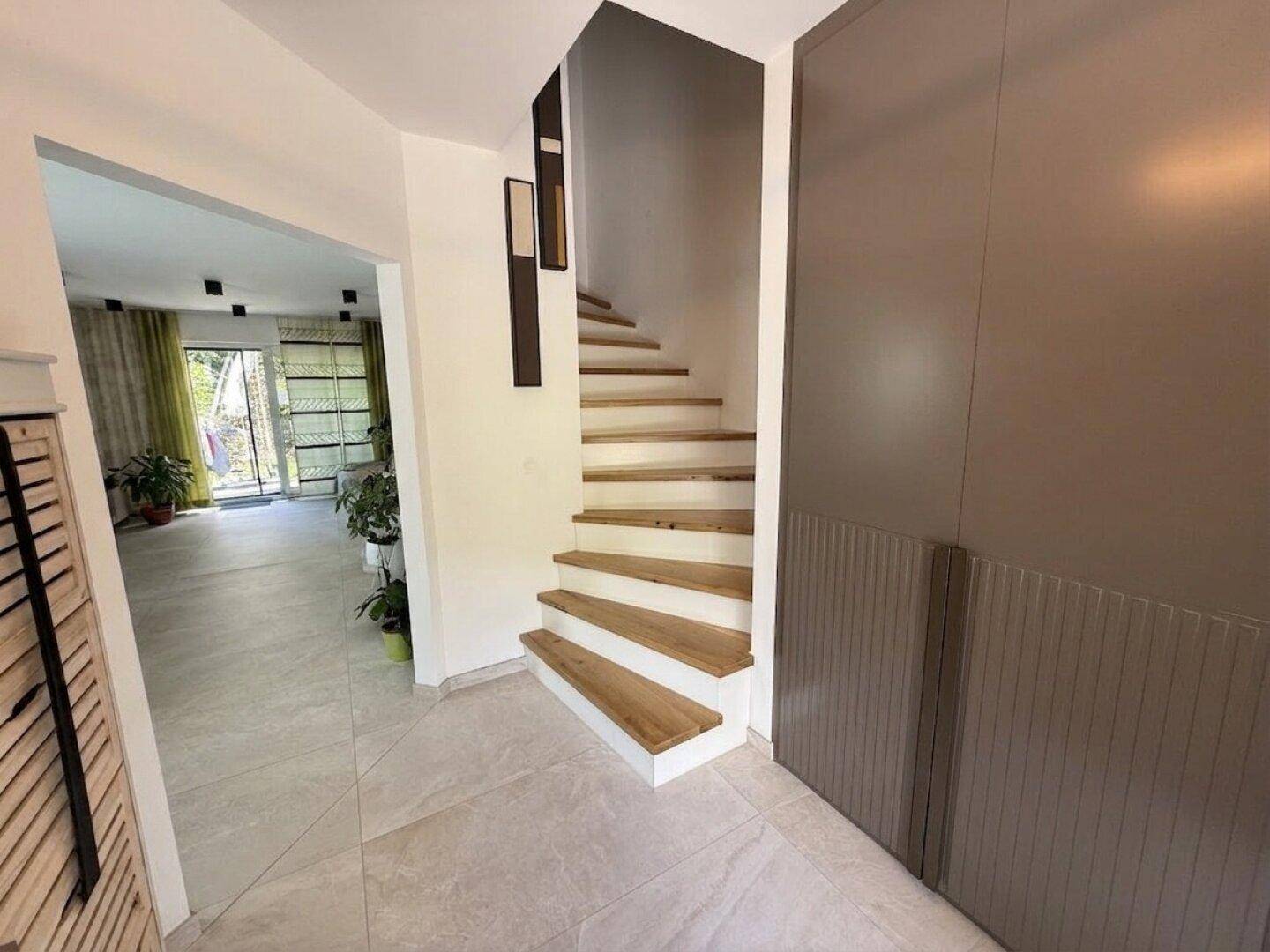 Heller Eingangsbereich mit moderner Holztreppe und großformatigen Fliesen auf dem Boden.