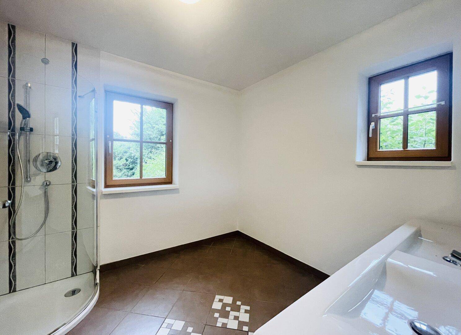Funktionales Badezimmer mit Eckdusche, Einzelwaschbecken und Blick ins Grüne.