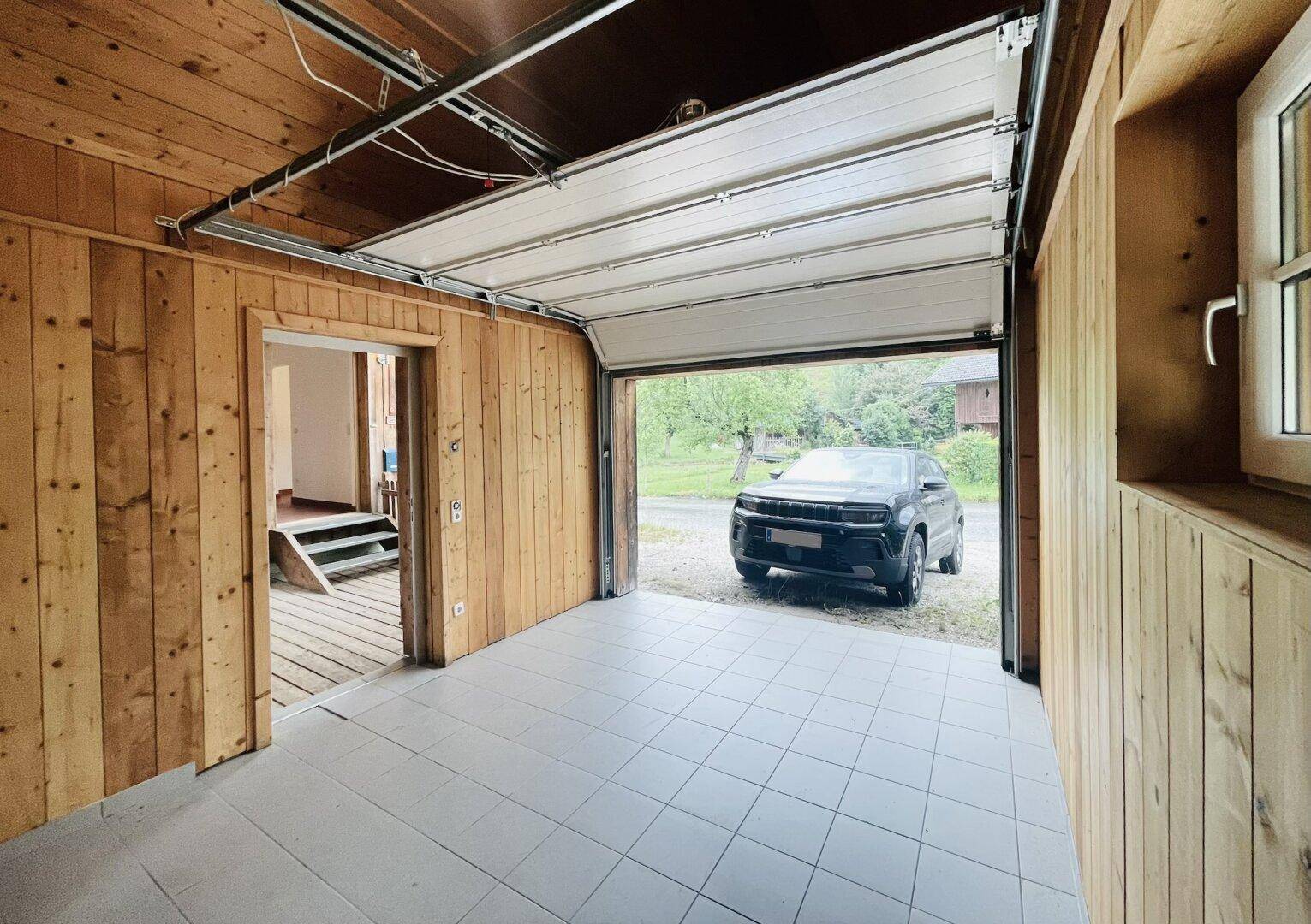 Geräumige Garage mit Holzverkleidung, Fliesenboden und offenem Tor zur Einfahrt.