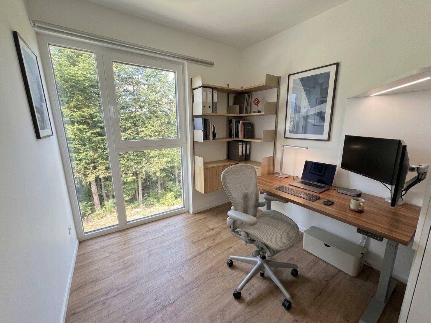 Modernes Arbeitszimmer mit großem Fenster, Holzboden und Blick auf die umliegende Natur.