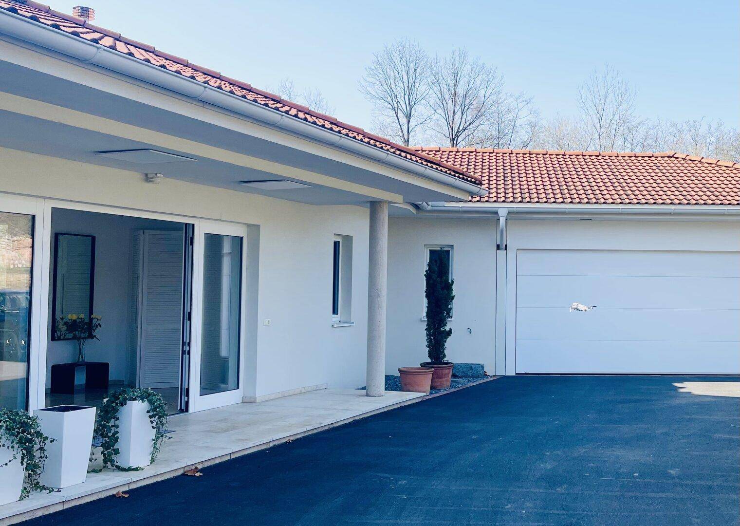 Modernes Einfamilienhaus mit weißer Fassade, Garage und gepflasterter Zufahrt.