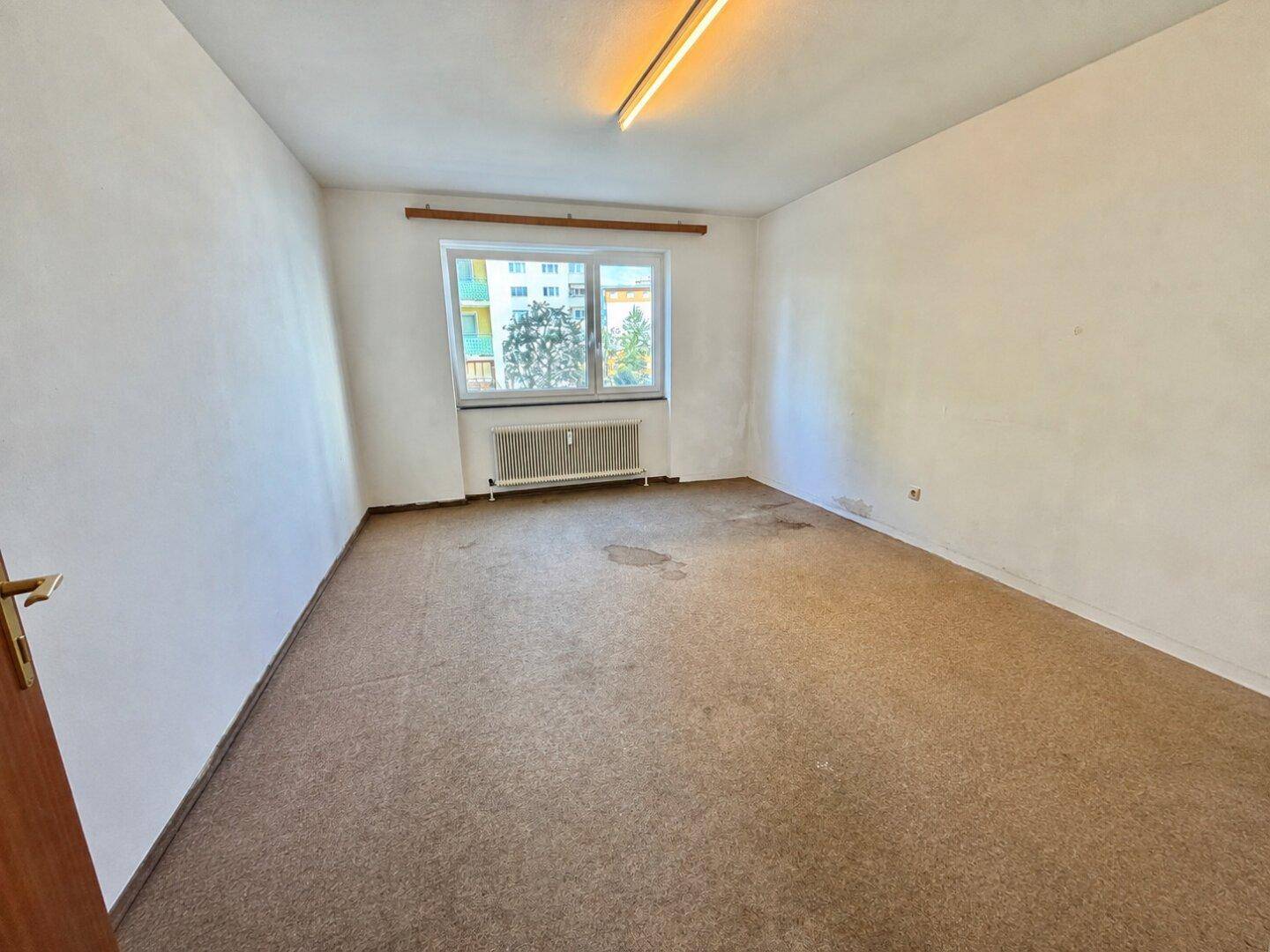 Unmöbliertes Zimmer mit Teppichboden und Fenster, das auf die Straße blickt.