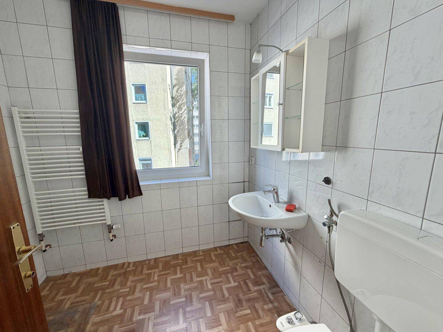 Gefliestes Badezimmer mit Waschbecken, Toilette, Bidet und Fenster.
