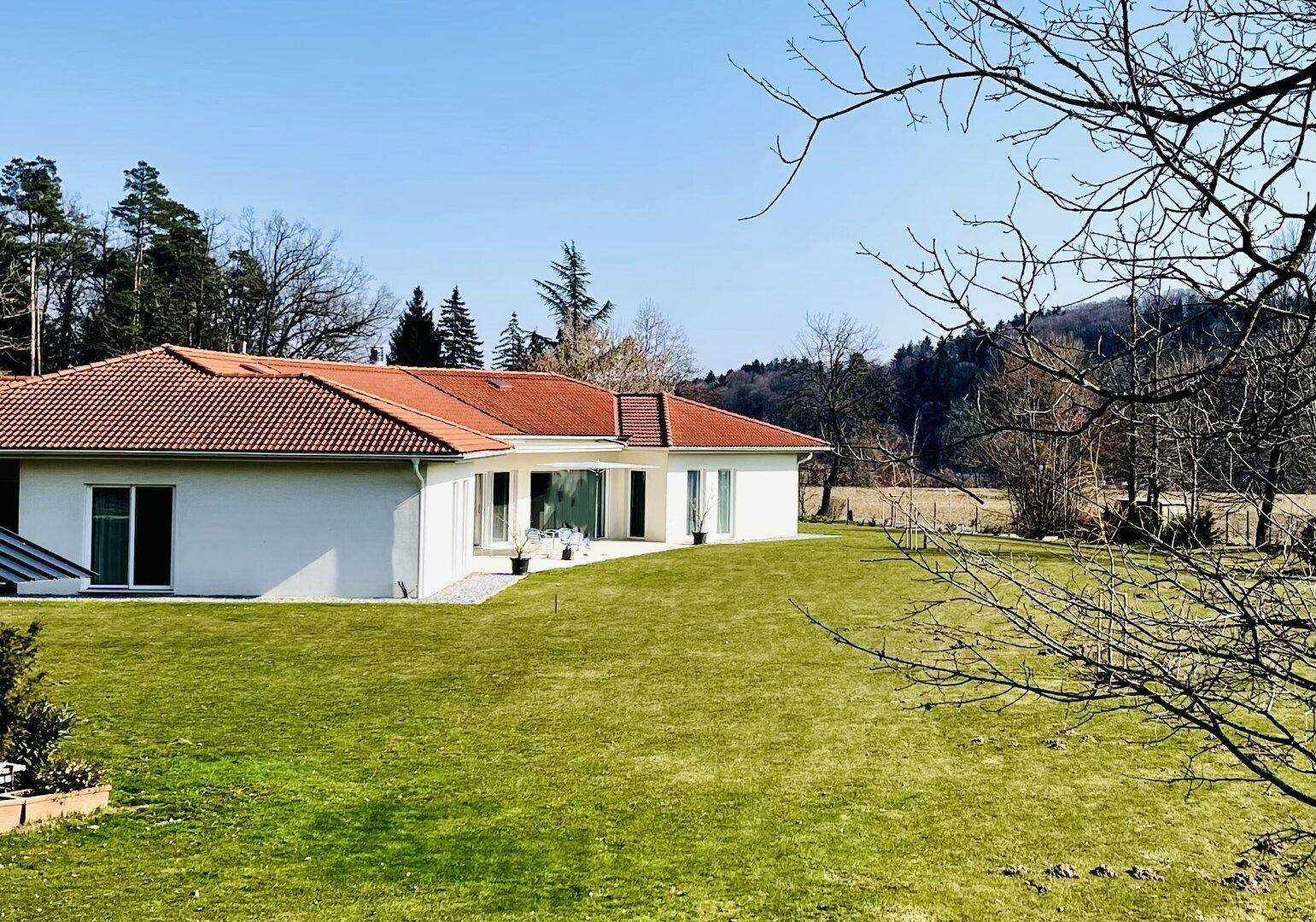 Modernes Haus mit rotem Ziegeldach und weitläufigem grünen Rasen in ländlicher Umgebung.