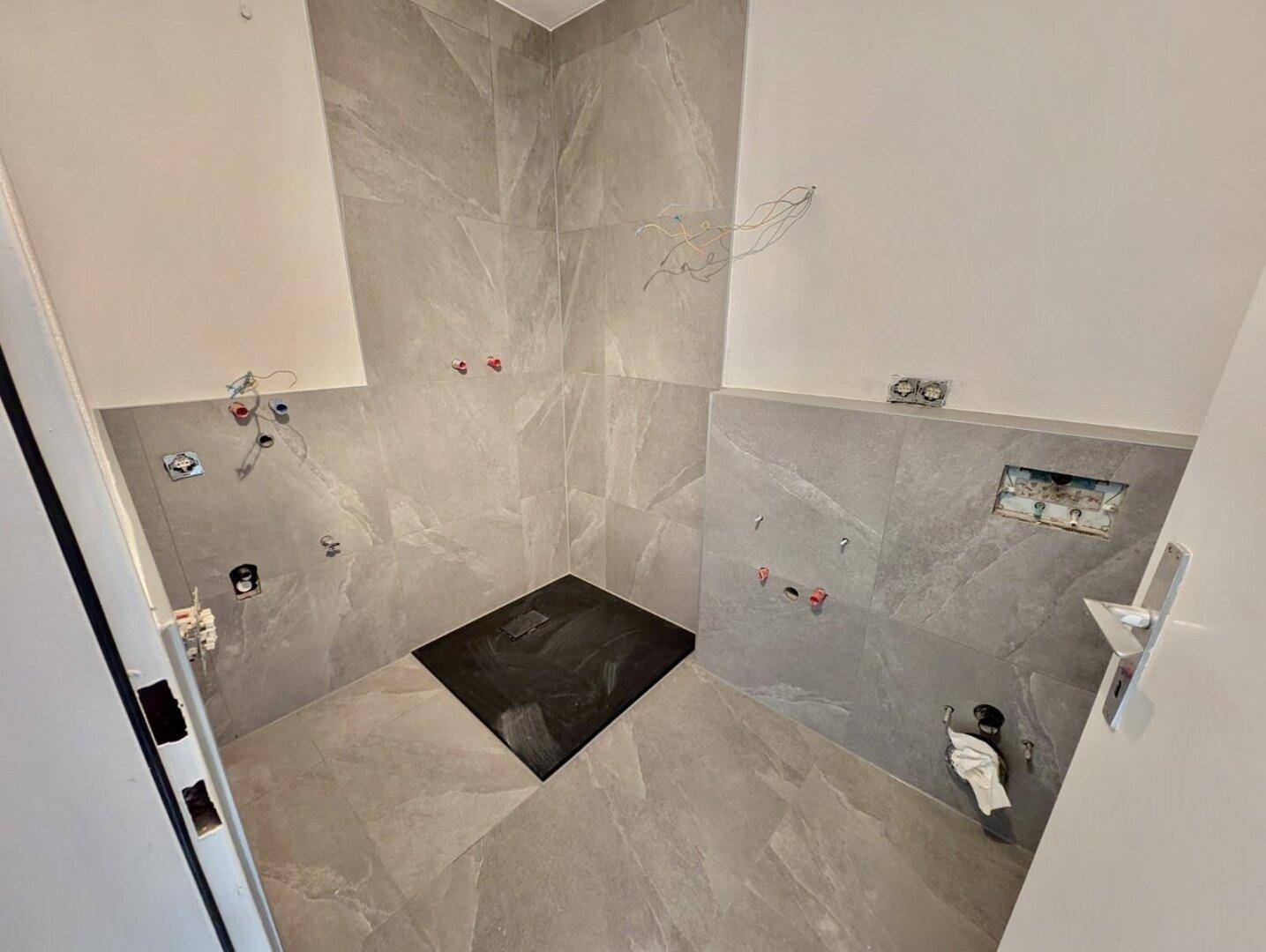 Modernes Badezimmer im Bau mit grauen Fliesen und vorbereiteter Duschfläche.