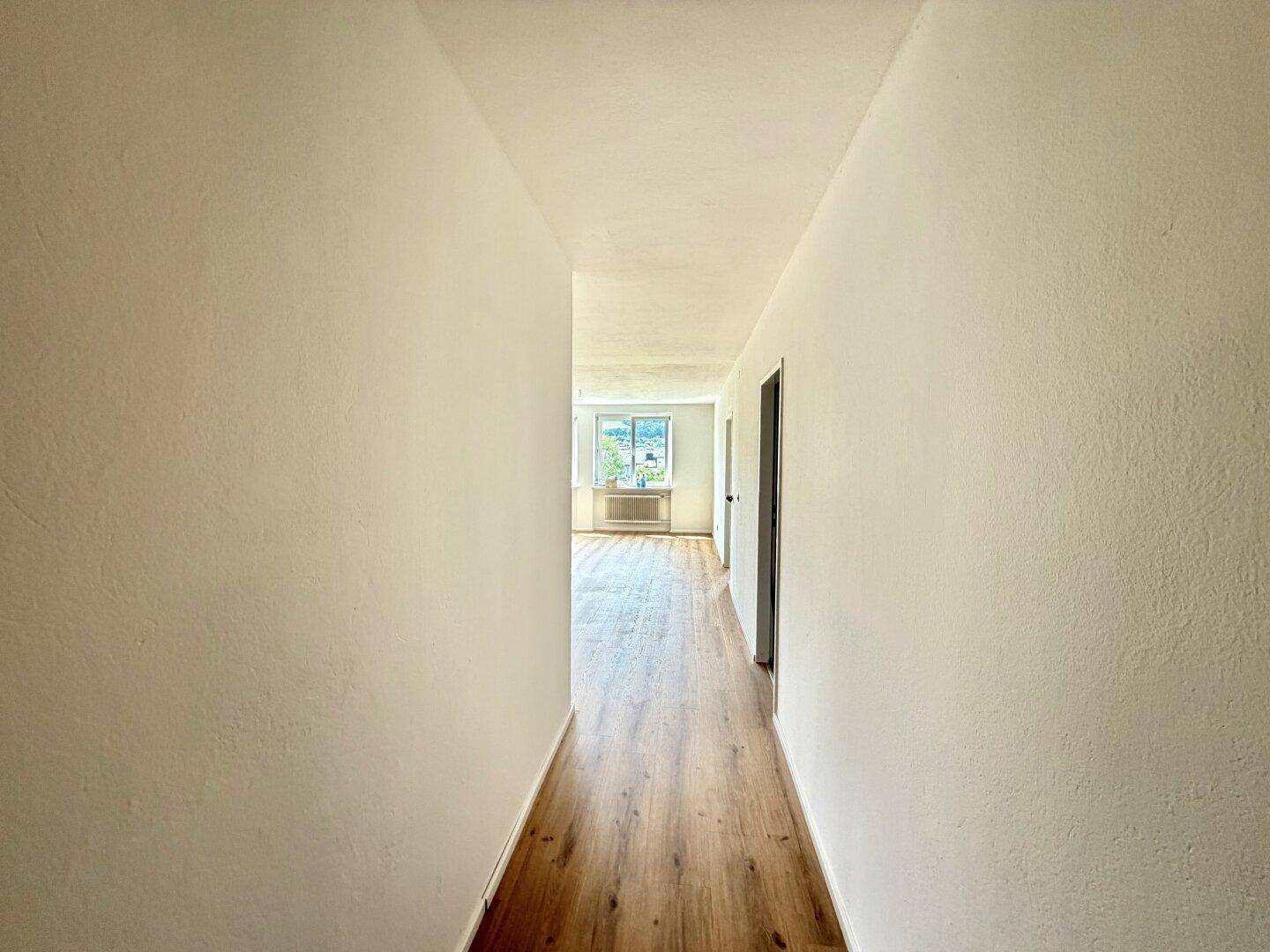 Heller Flur mit Laminatboden, der zu einem weiteren Raum mit Fenstern führt.