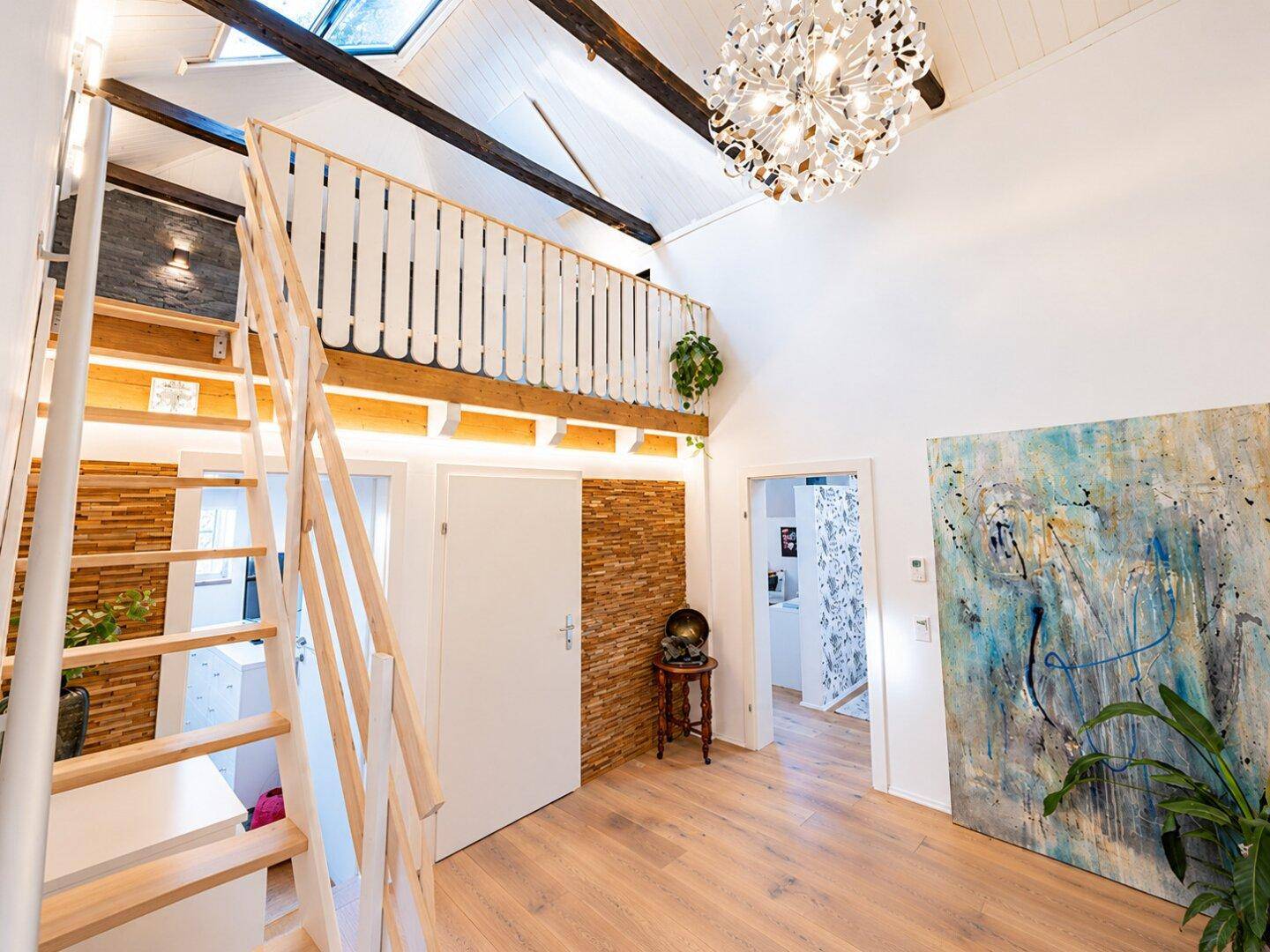 Heller Eingangsbereich mit Treppe zur Galerie, Holzwand und moderner Beleuchtung.
