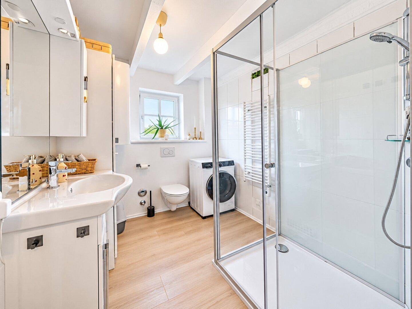 Helles Badezimmer mit Dusche, Waschmaschine und Fenster, ausgestattet mit modernen Armaturen.