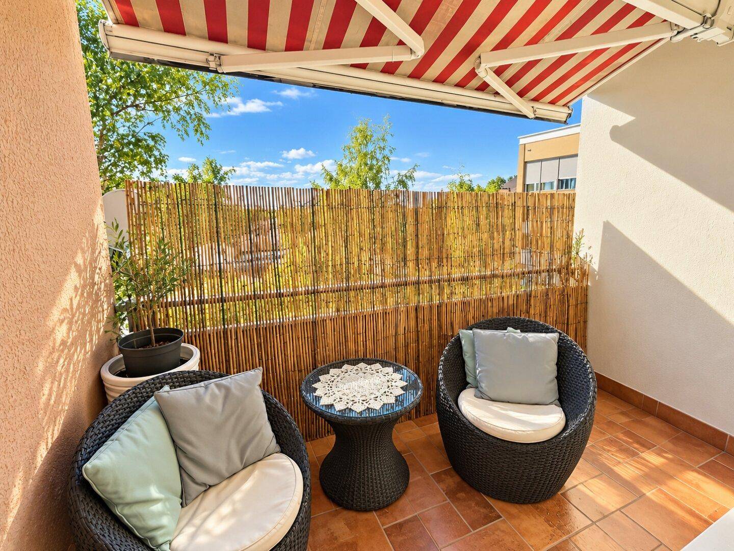 Gemütlicher Balkon mit Markise, Rattanmöbeln und Sichtschutz für entspannte Stunden.
