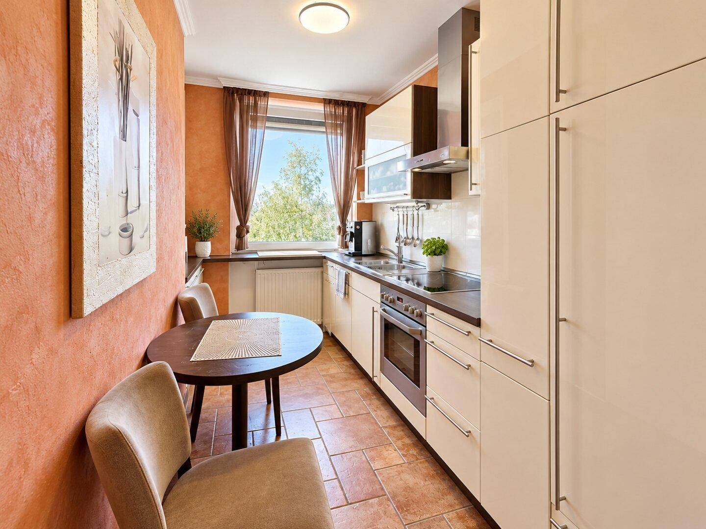 Funktionale Küche mit Einbaugeräten, kleinem Esstisch und Fenster für Tageslicht.