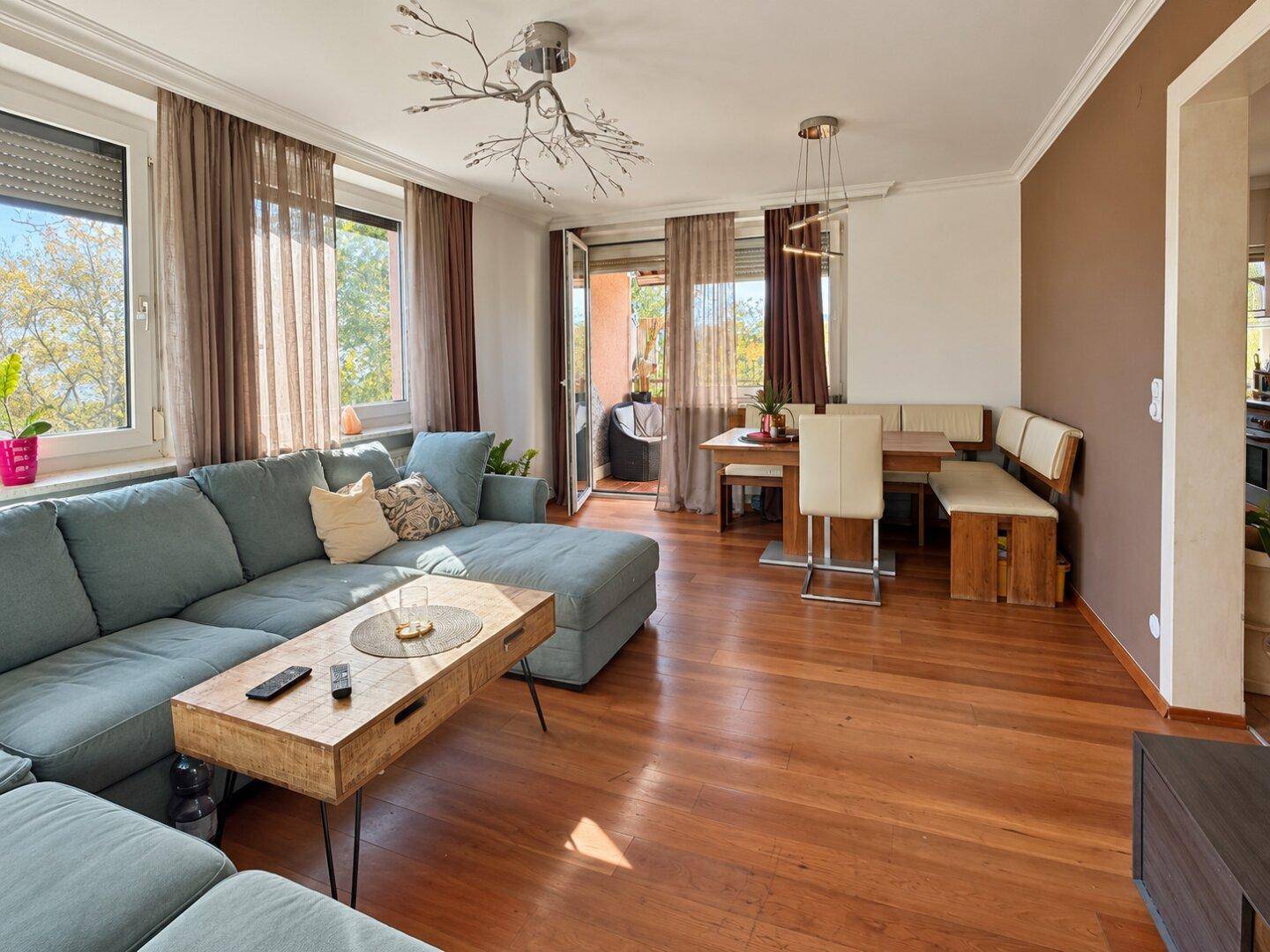 Heller Wohn-Essbereich mit Zugang zum Balkon, Holzboden und gemütlicher Sitzecke.
