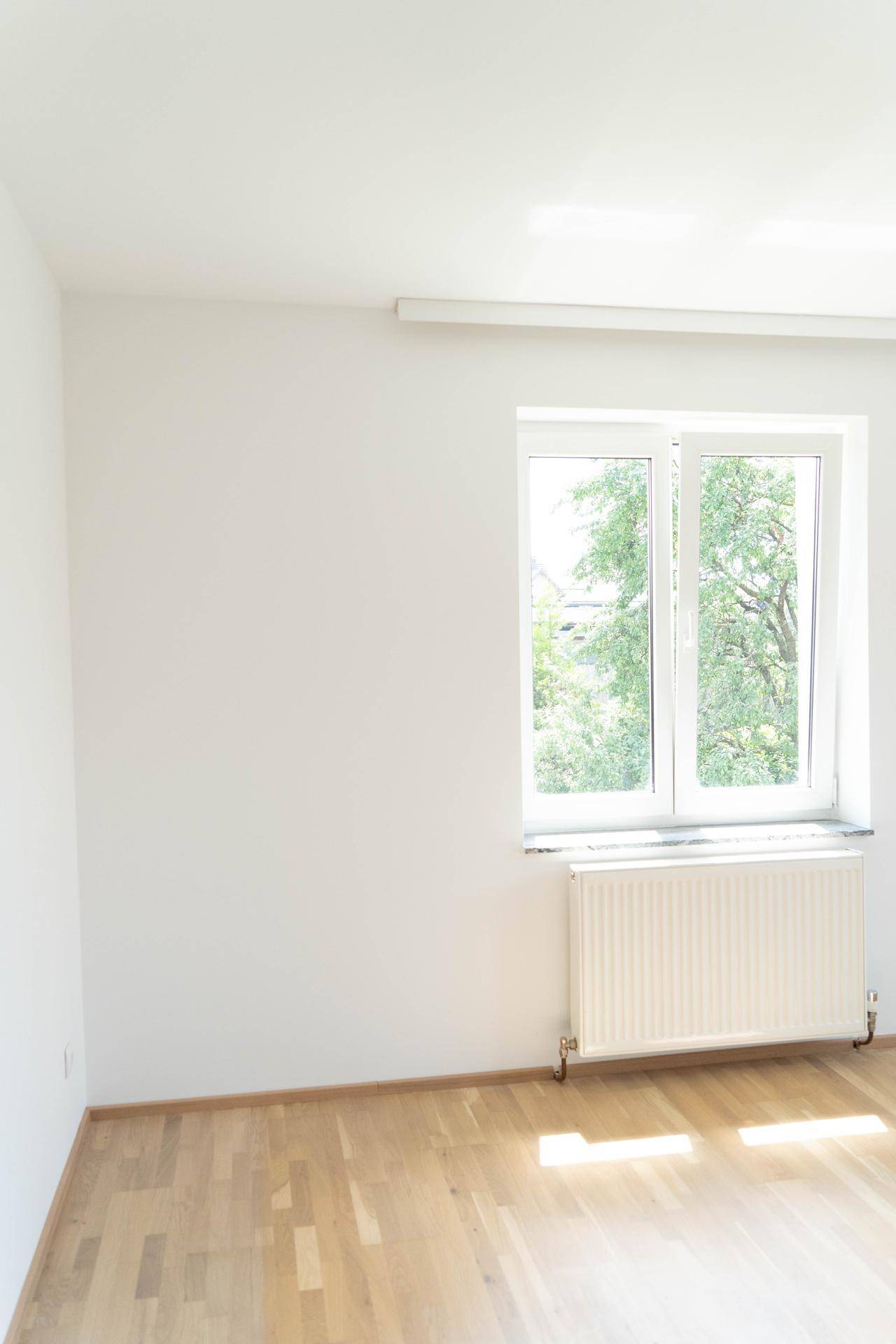 Helles Zimmer mit Parkettboden, einem Fenster und viel natürlichem Sonnenlicht.