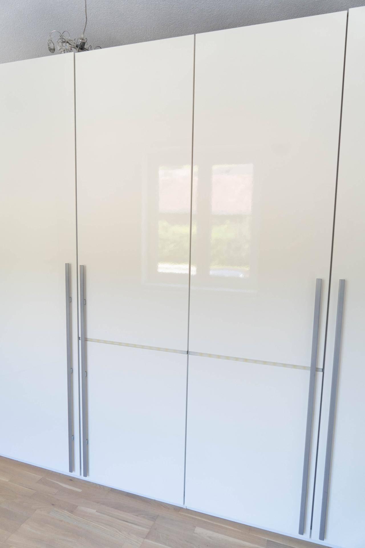Großer, weißer Hochglanz-Kleiderschrank mit modernen Griffen und Fensterreflexionen.