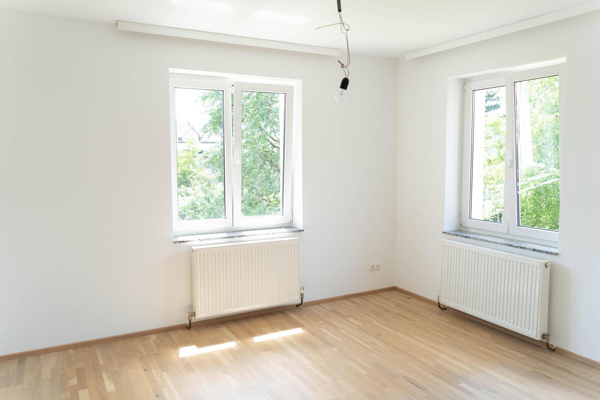Großes, helles Zimmer mit zwei Fenstern, Parkettboden und Heizkörpern, ideal für Wohnzwecke.