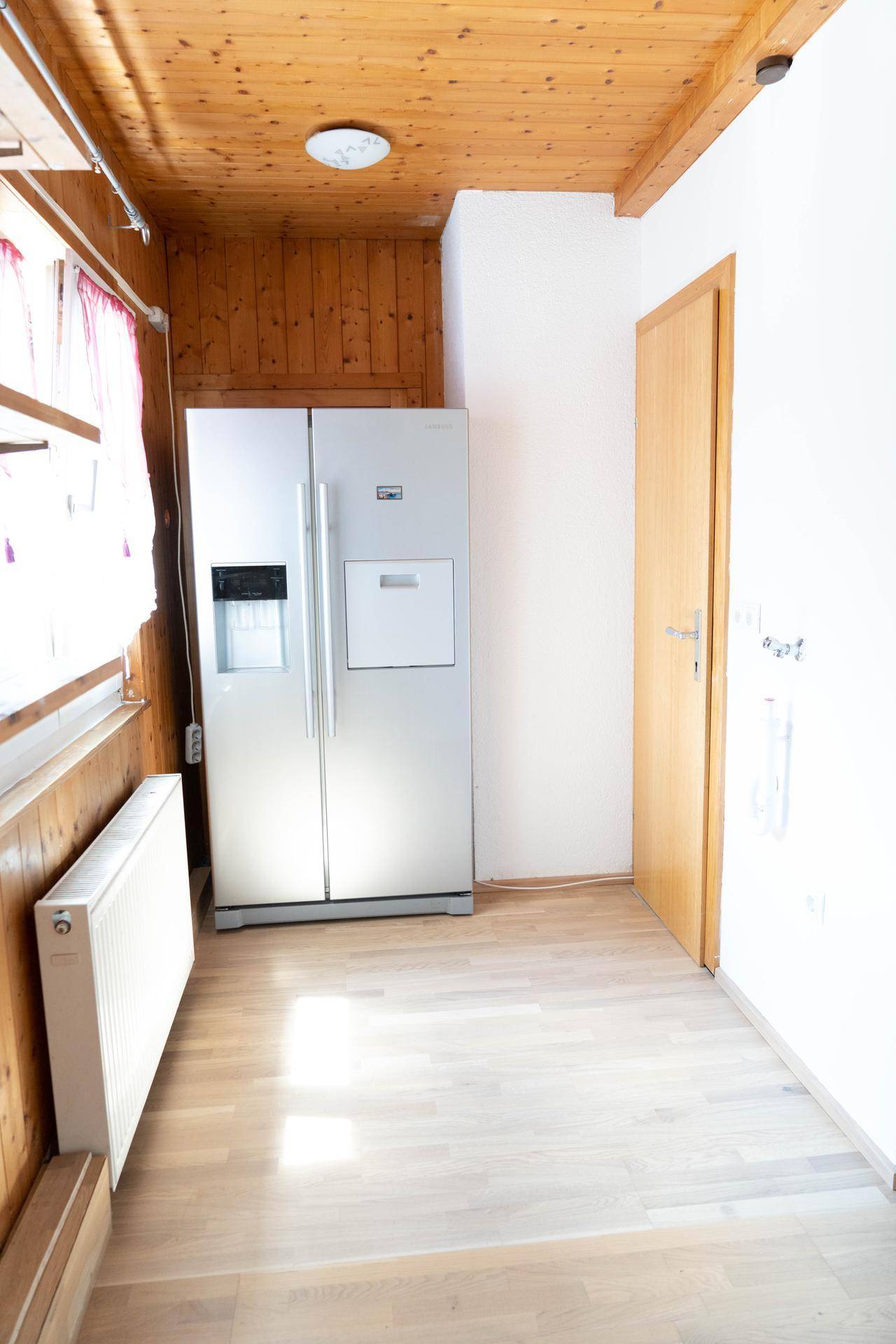 Bereich mit großem Kühlschrank, Holzwänden und -decke, sowie hellem Parkettboden.