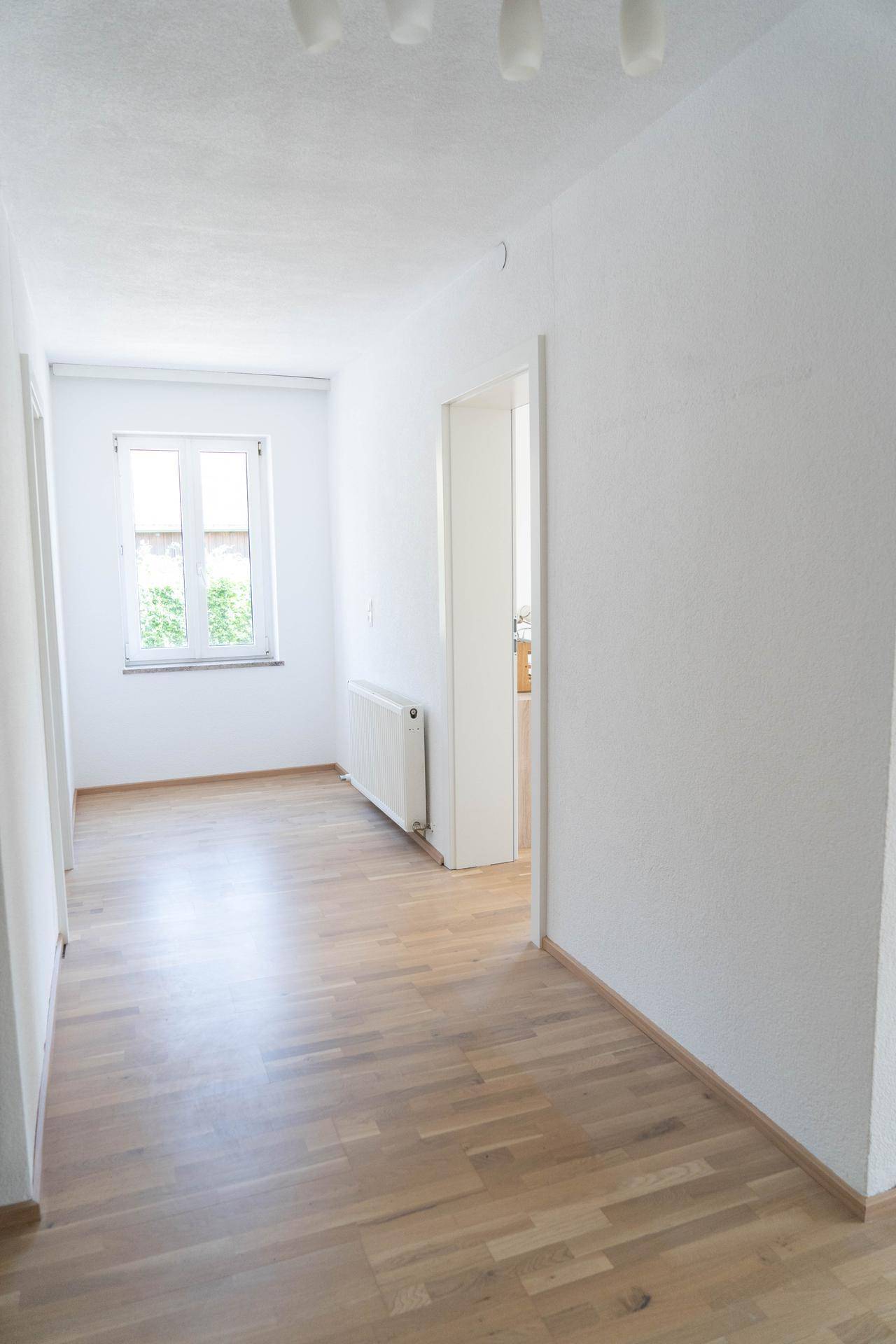 Langer, heller Flur mit Parkettboden und Fenster am Ende, das Tageslicht hereinlässt.