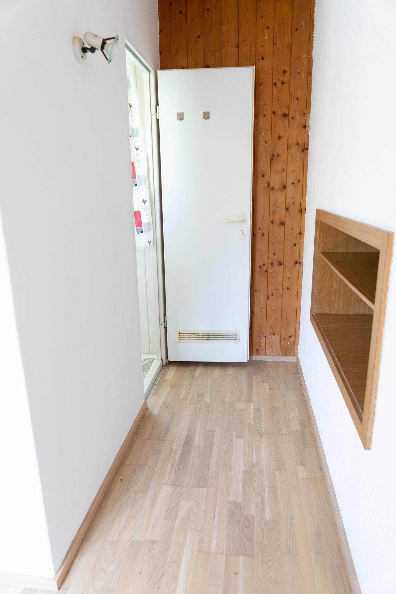 Flur mit Holzwandverkleidung und hellem Parkettboden, der zum Badezimmer führt.