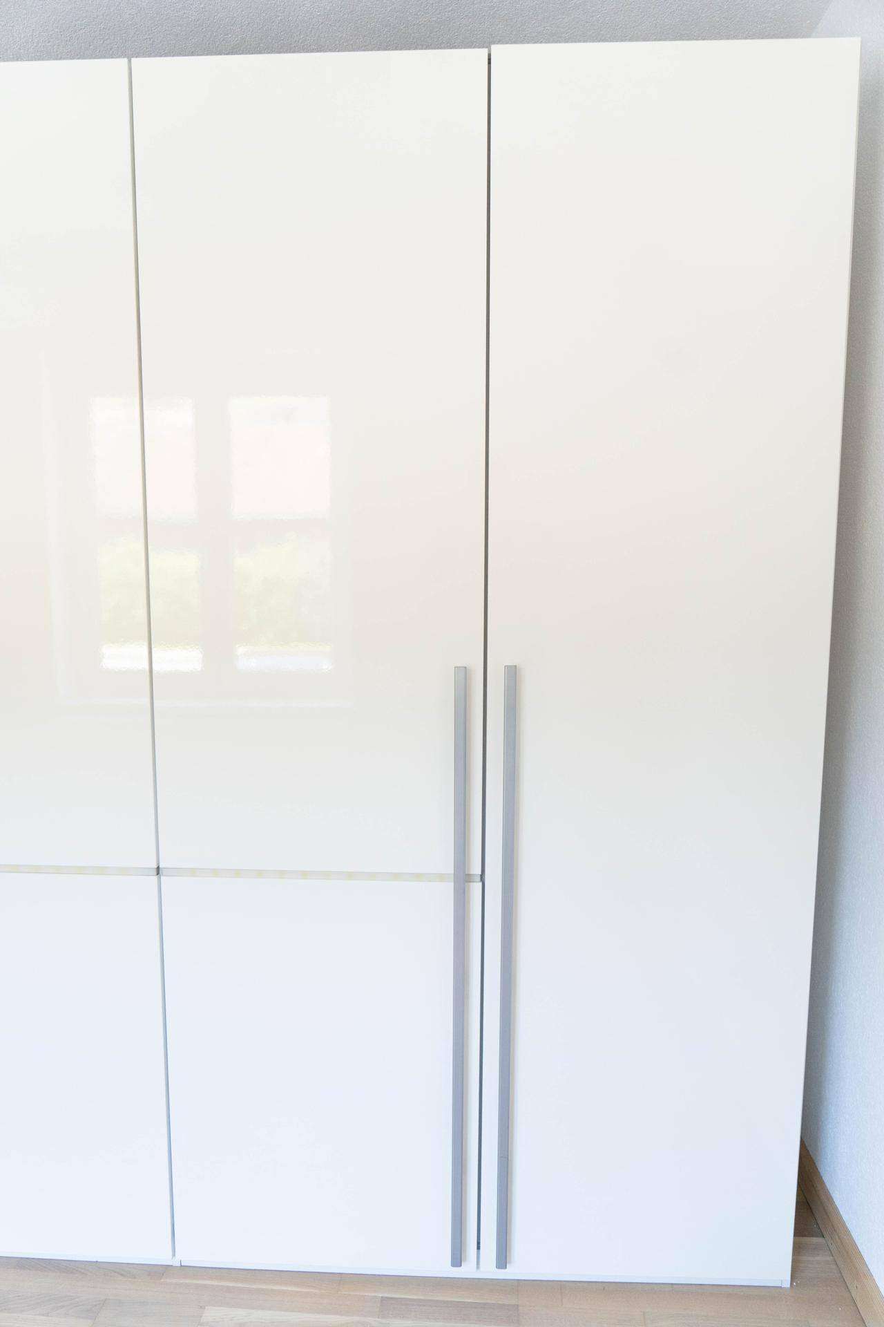 Moderner, weißer Kleiderschrank mit glänzender Oberfläche, der viel Stauraum bietet.