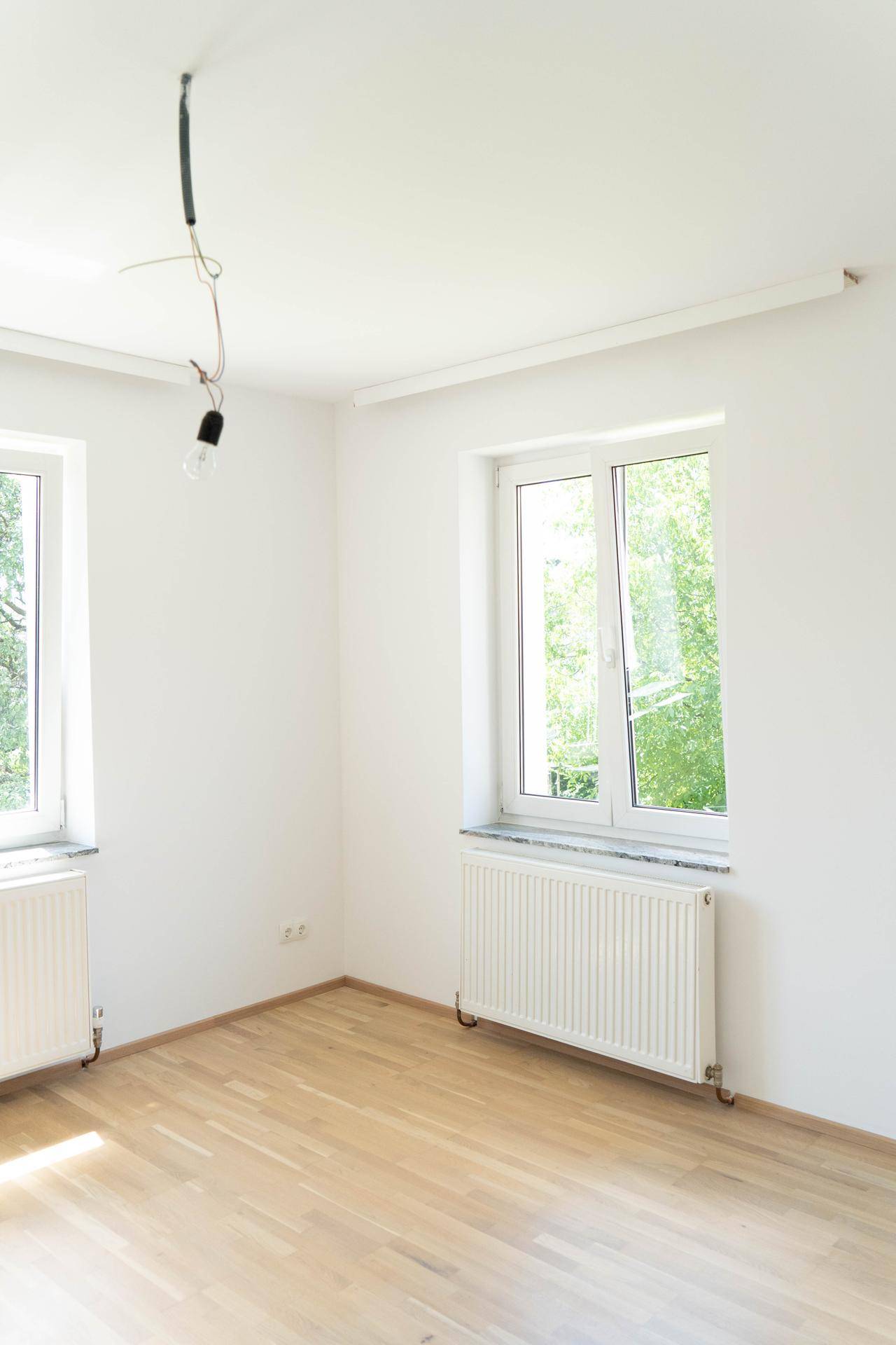 Helles Zimmer mit Parkettboden, einem Fenster und Heizkörper, das viel Tageslicht erhält.
