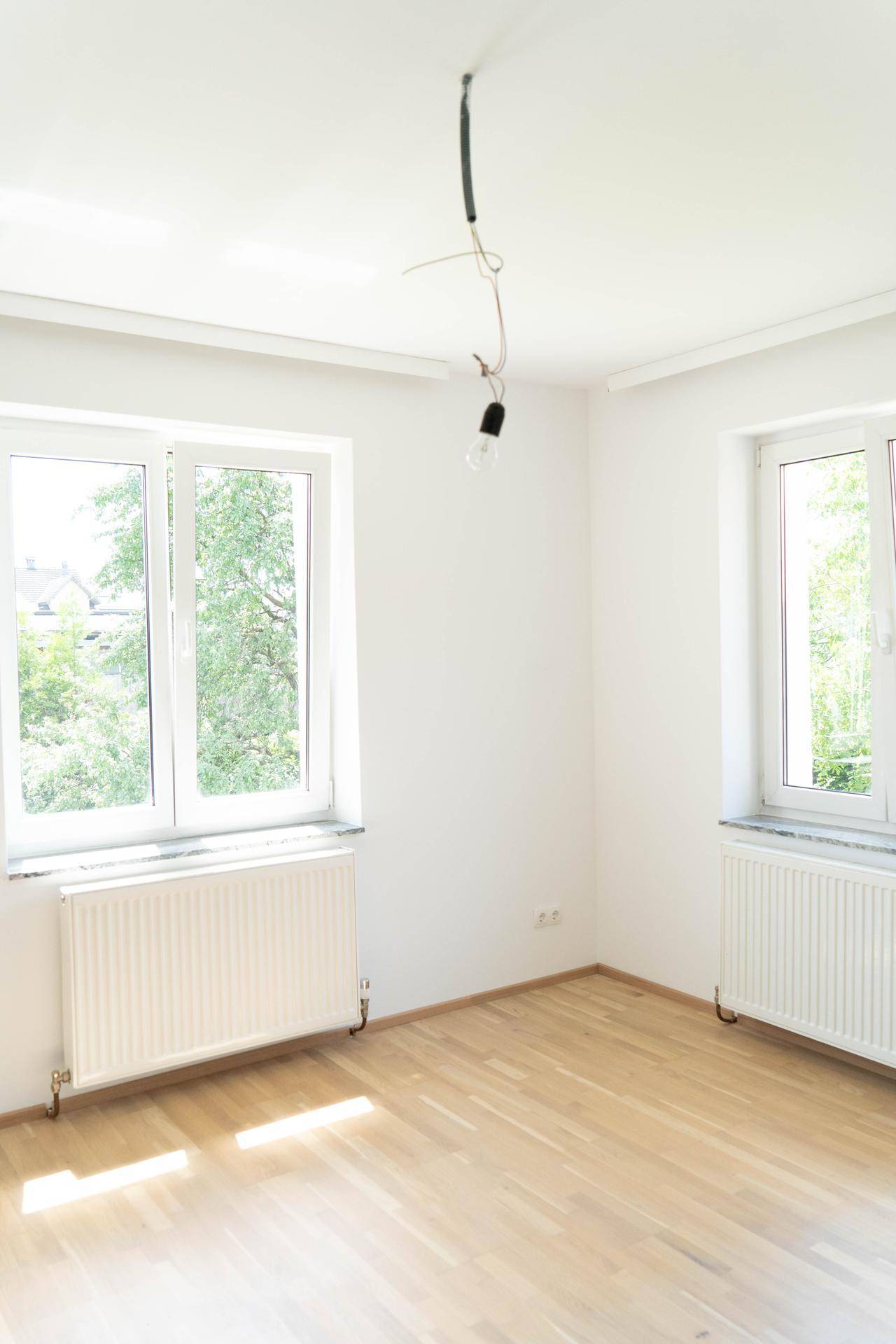 Geräumiges, helles Zimmer mit zwei Fenstern, Parkettboden und Heizkörpern, sehr einladend.