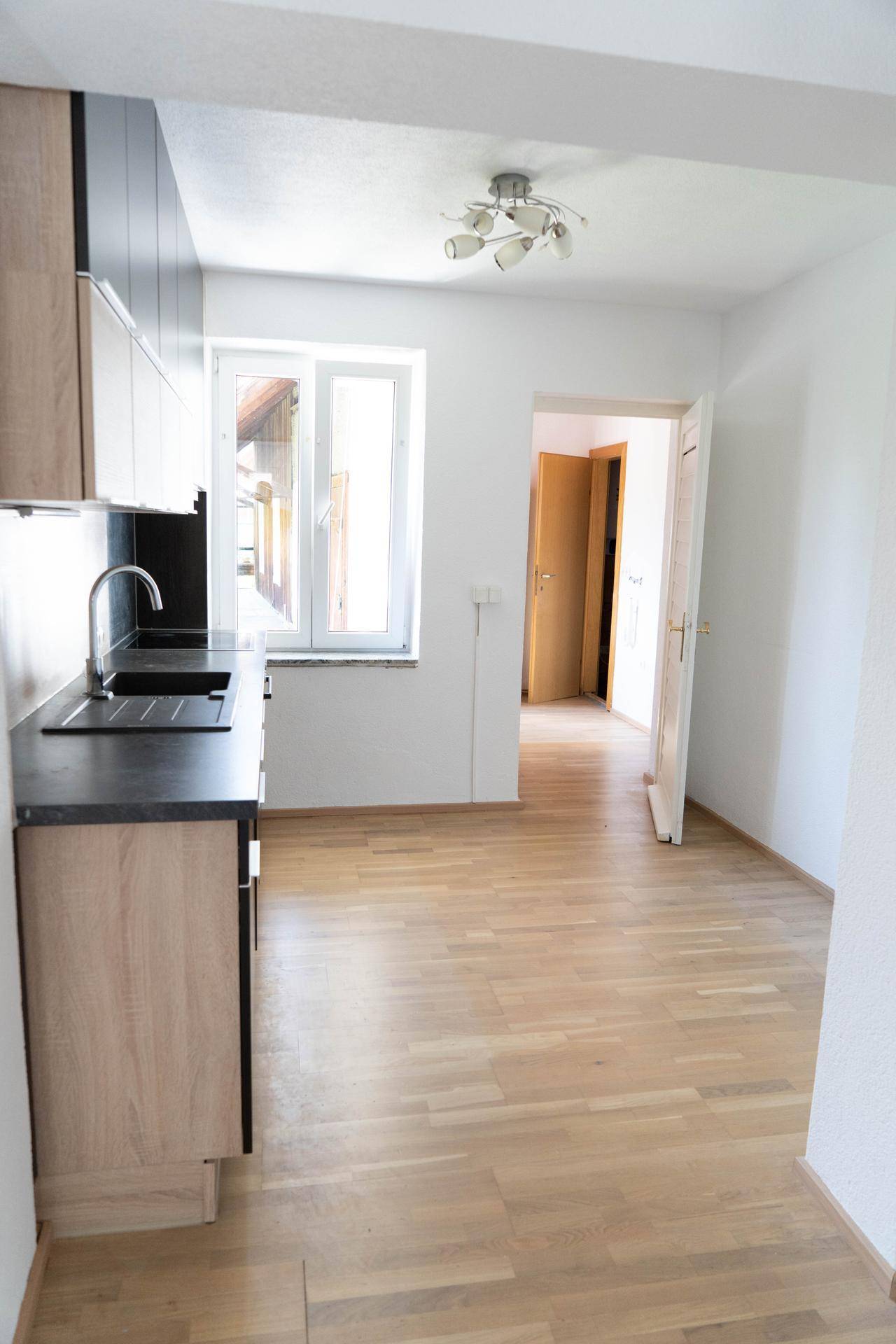 Moderne Küche mit Holz- und Schwarzfronten, Parkettboden und Zugang zu weiteren Räumen.