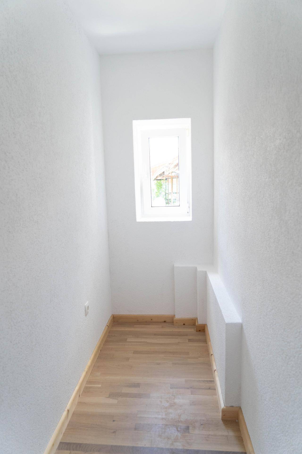 Schmaler Raum mit kleinem Fenster und Parkettboden, ideal als Abstell- oder Lagerraum.