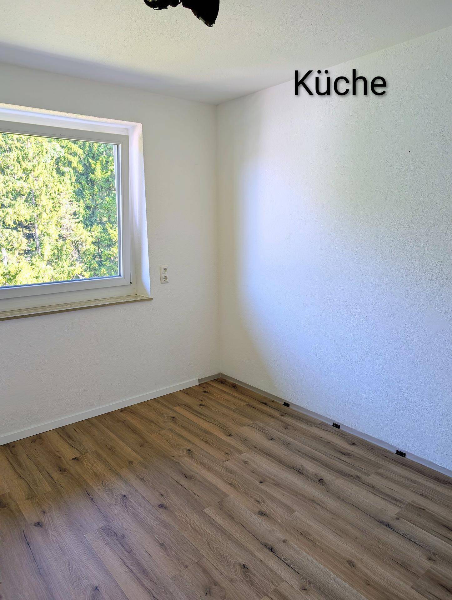 Leere Küche mit Laminatboden und Fenster, bereit für die Installation einer Einbauküche.