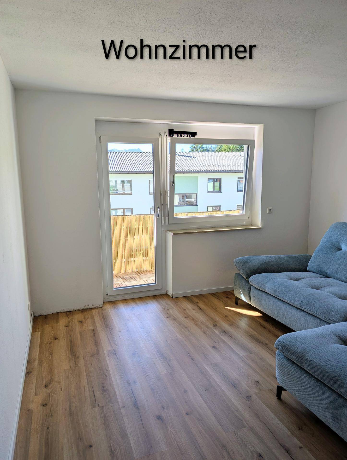 Wohnzimmer mit Laminatboden, Sofa und Fenster mit Blick auf die Umgebung.