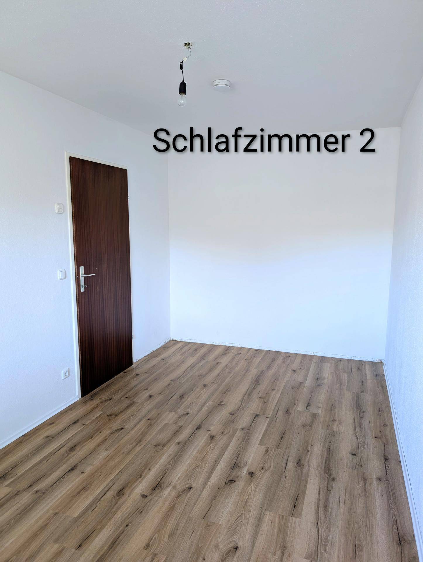 Weiteres Schlafzimmer mit Laminatboden und einer dunklen Holztür, ideal als Kinder- oder Gästezimmer.