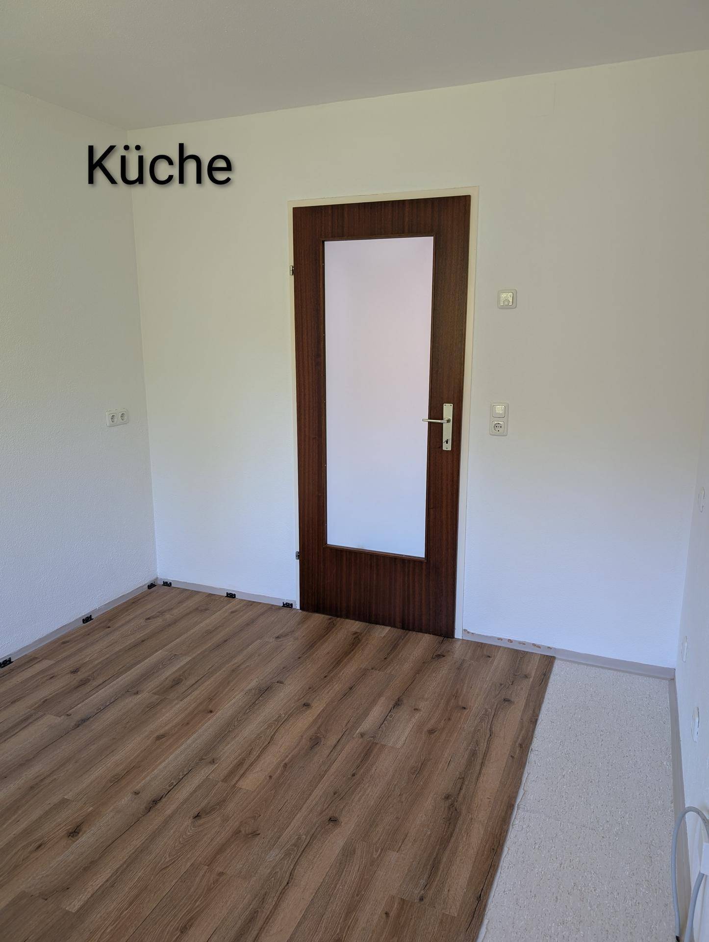 Leere Küche mit Laminatboden und einer modernen Holztür, bereit für die Einrichtung.