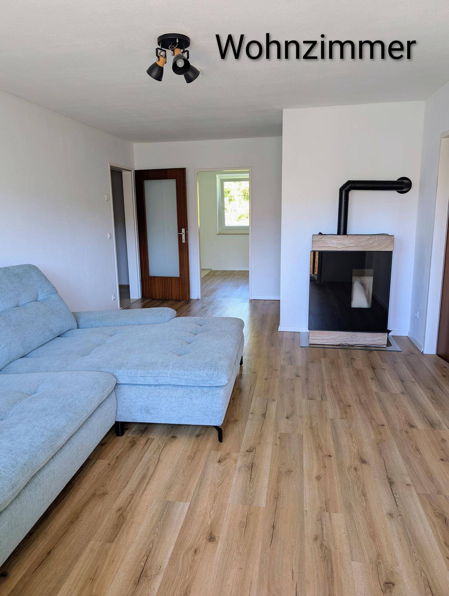 Gemütliches Wohnzimmer mit Laminatboden, modernem Sofa und einem Pelletofen.
