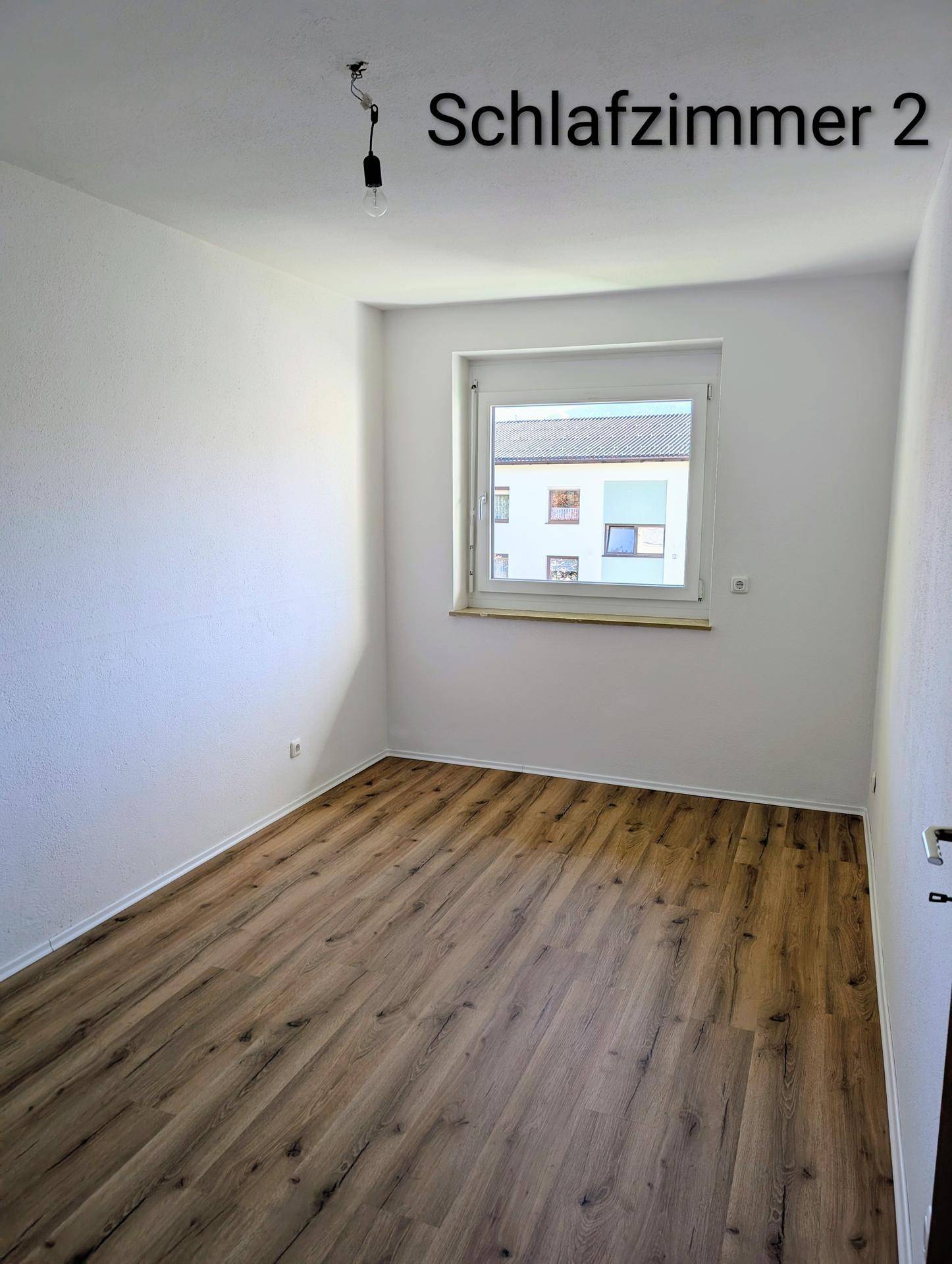 Helles Schlafzimmer mit Laminatboden und Fensterblick auf die umliegenden Gebäude, gut belichtet.