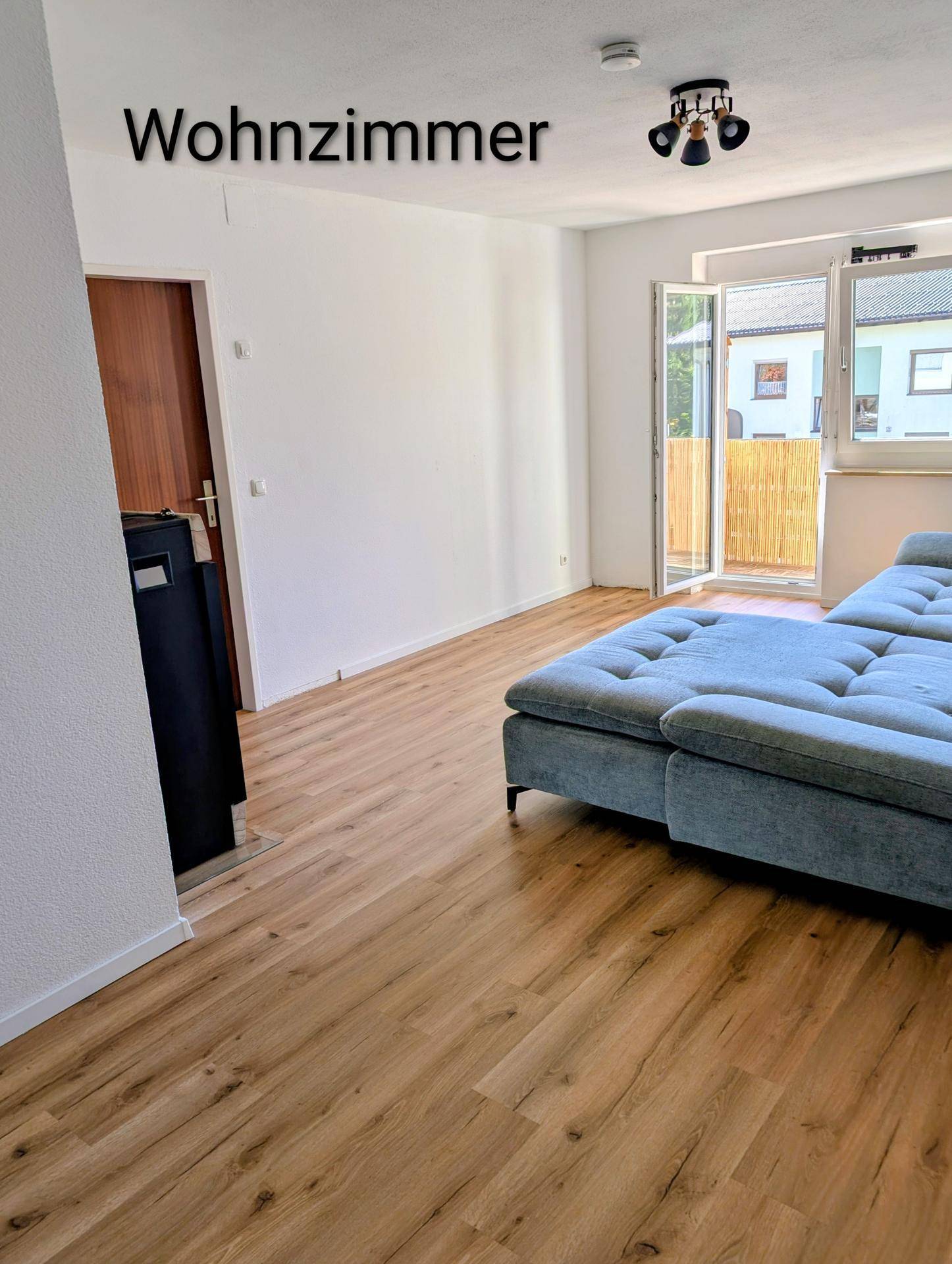 Helles Wohnzimmer mit Laminatboden, modernem Sofa und Zugang zum Balkon.