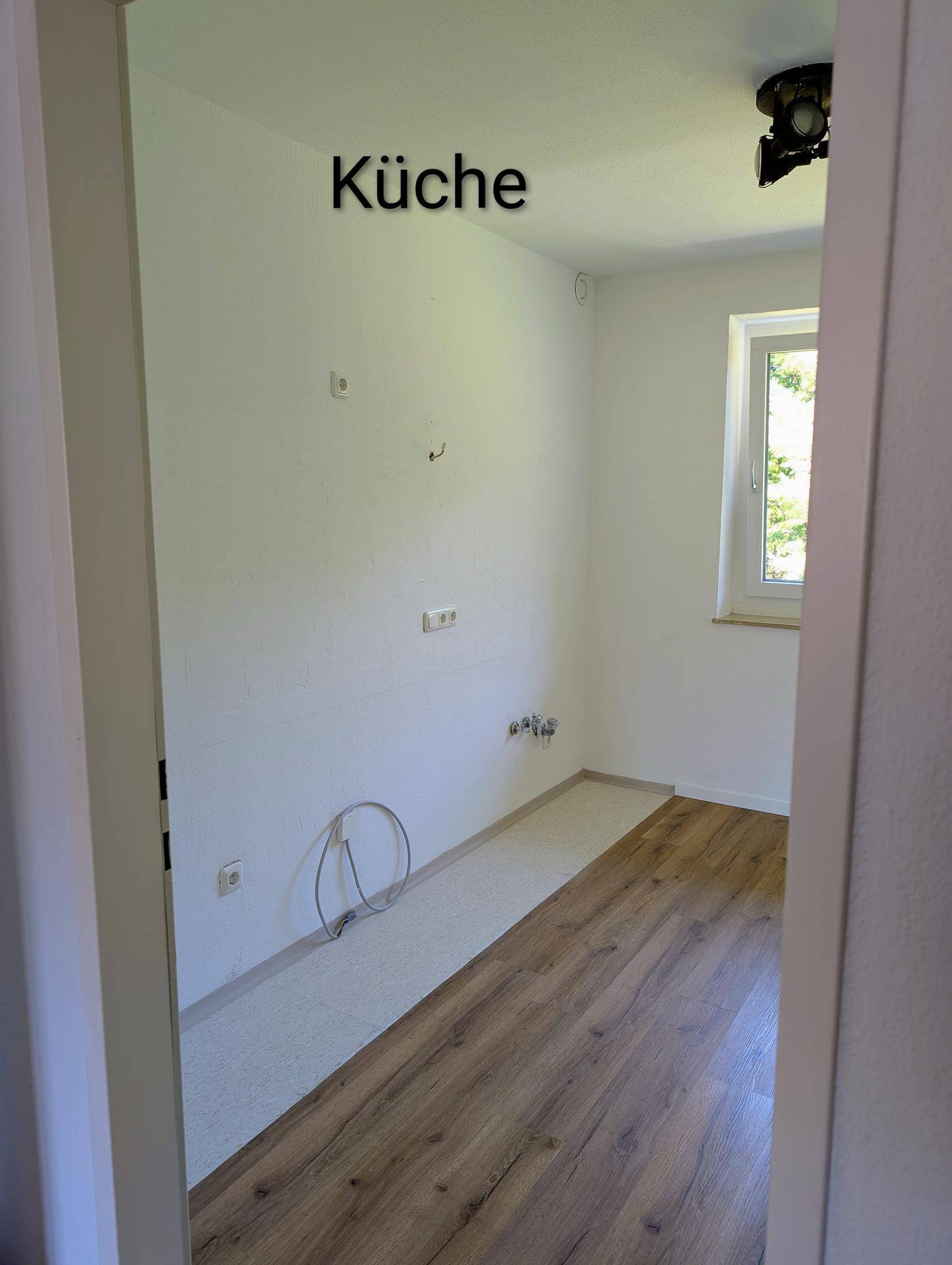 Leere Küche mit Laminatboden und Anschlüssen für eine zukünftige Kücheninstallation.
