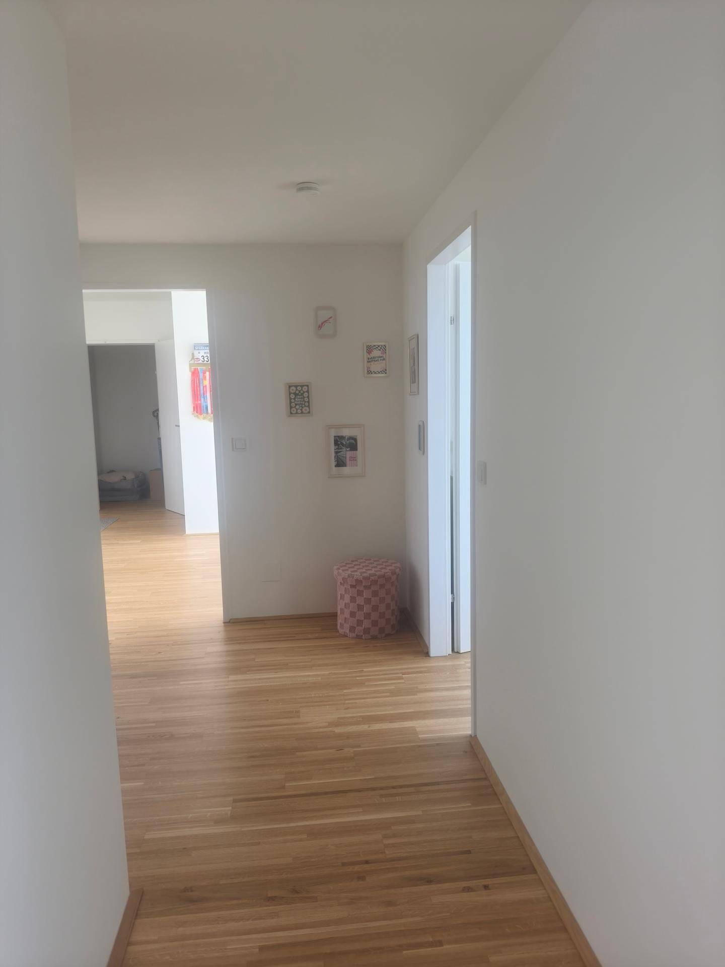 Langer, heller Flur mit Holzboden und schlichter Wanddekoration, der zu weiteren Räumen führt.