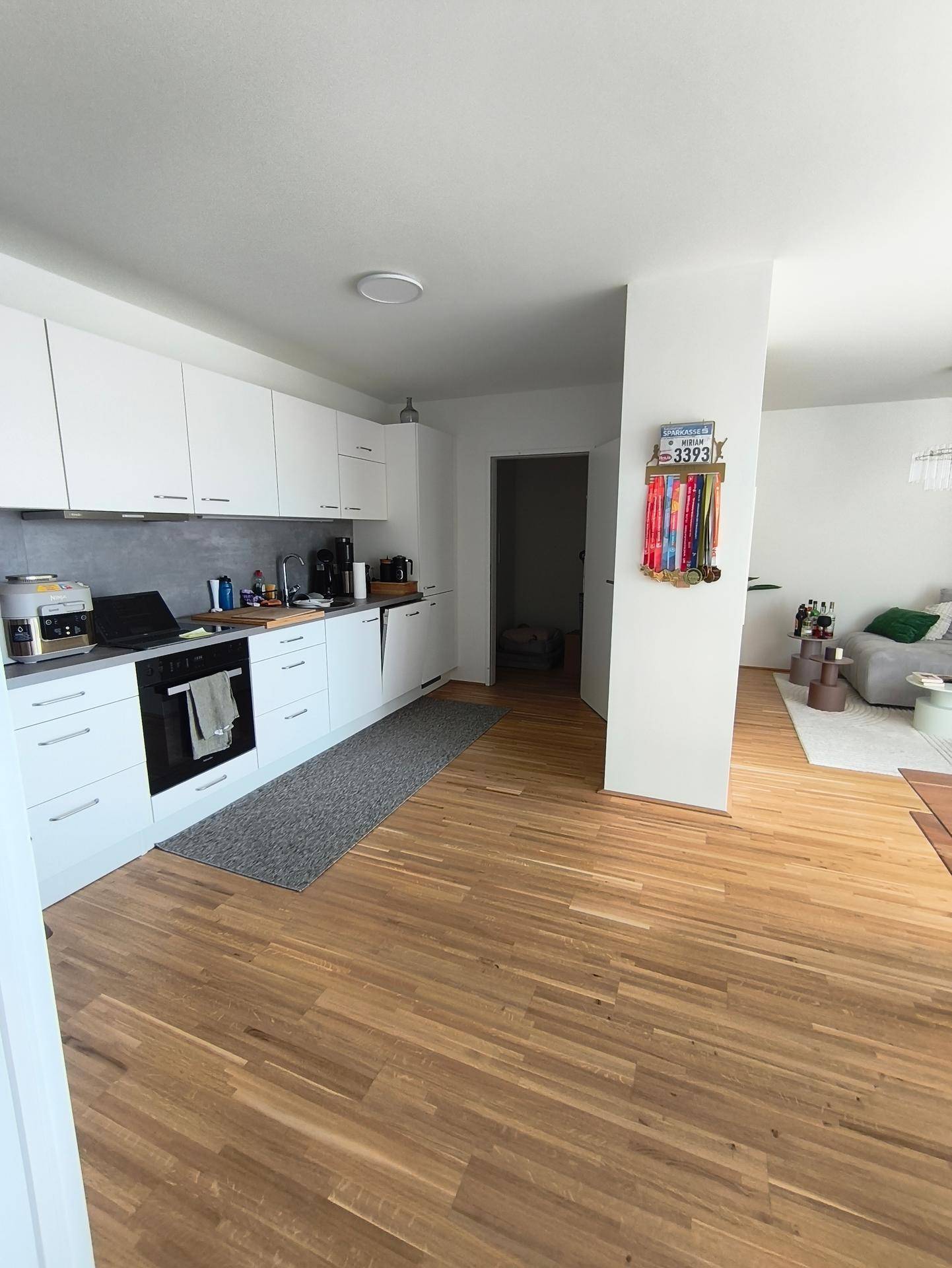 Moderne offene Küche mit weißen Schränken, Holzboden und integrierten Geräten.