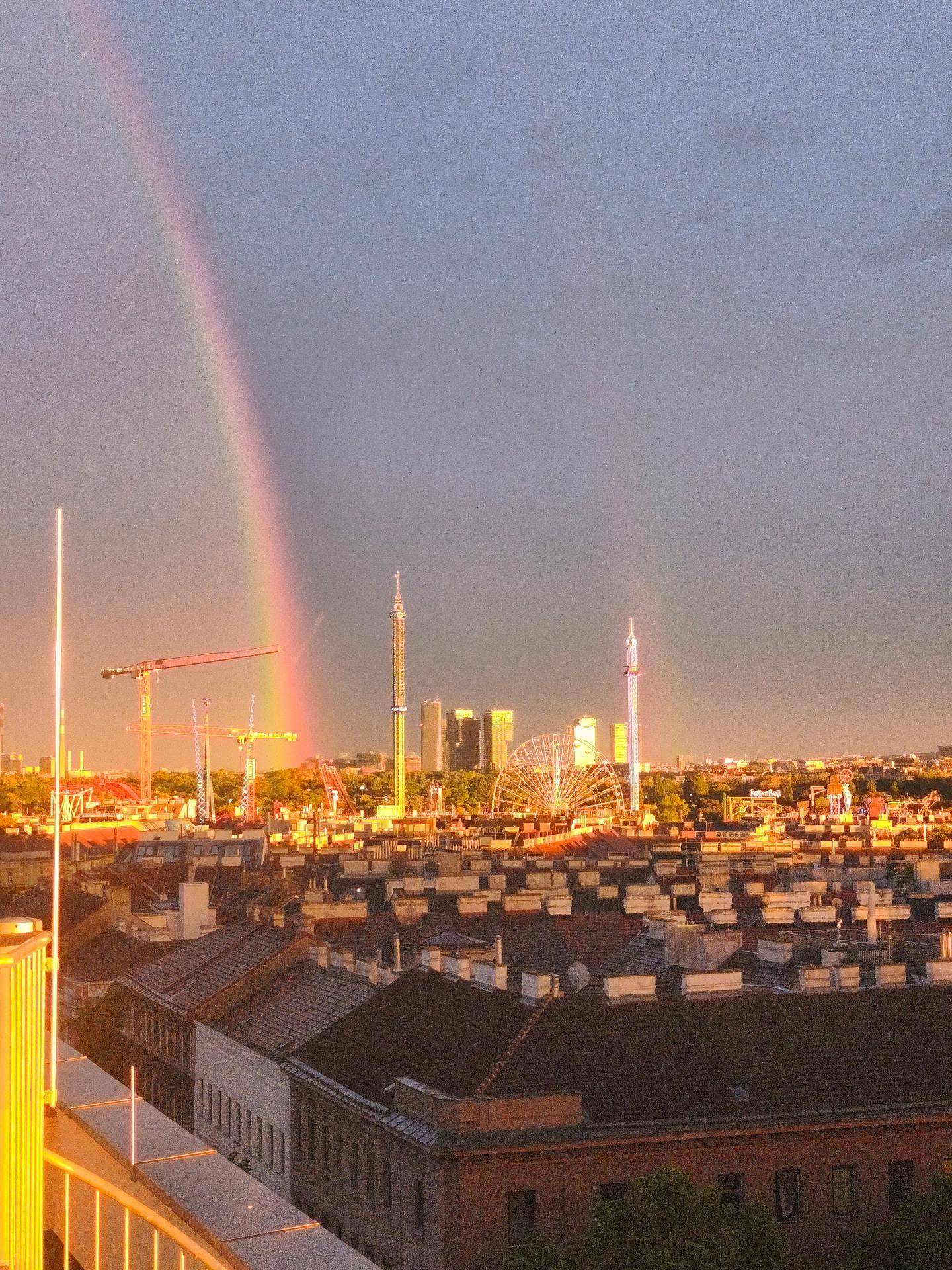 Panoramablick über die Stadt bei Sonnenuntergang mit einem beeindruckenden Regenbogen am Himmel.