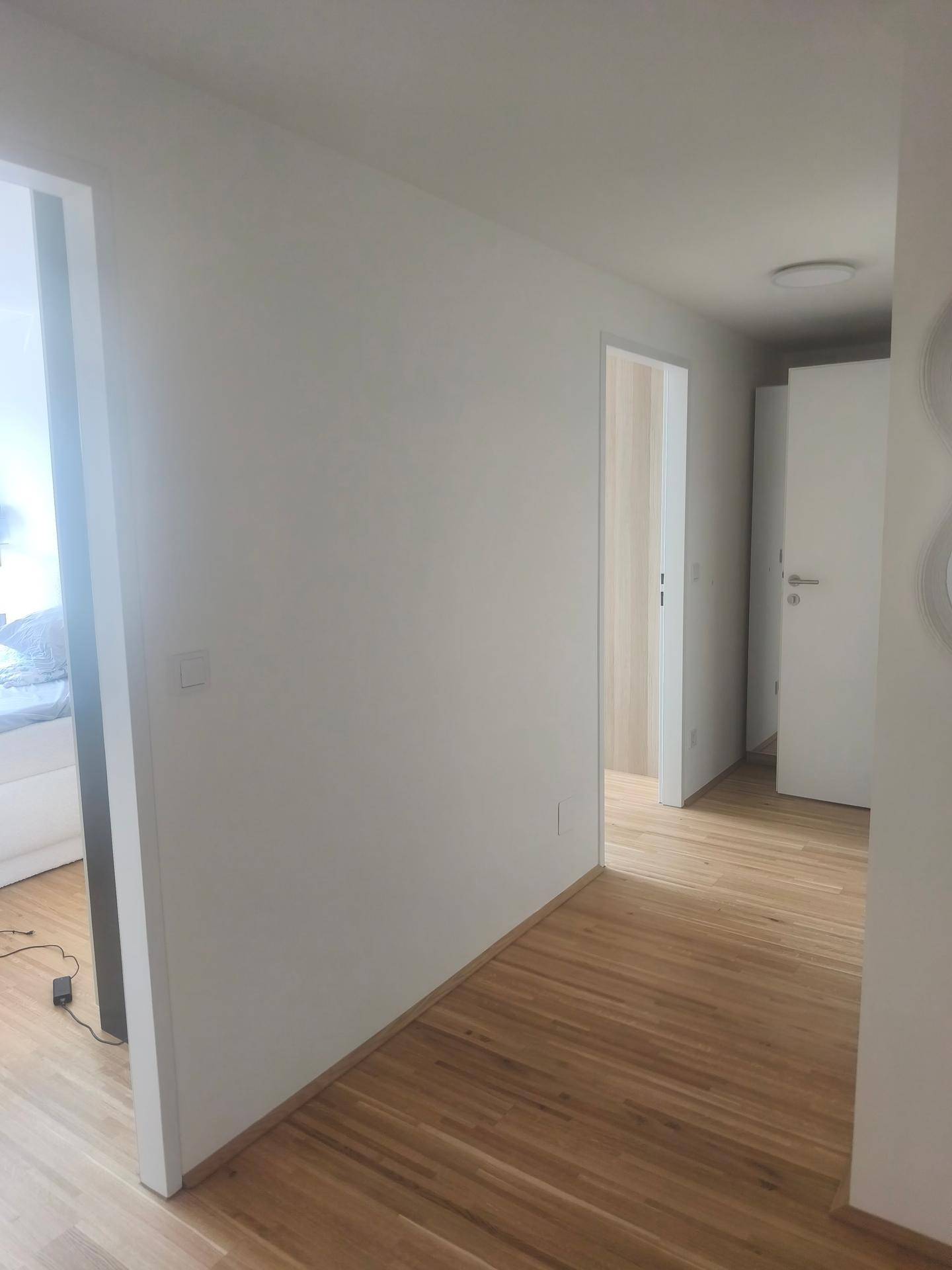 Heller Flur mit Holzboden und weißen Wänden, der zu verschiedenen Zimmern führt.