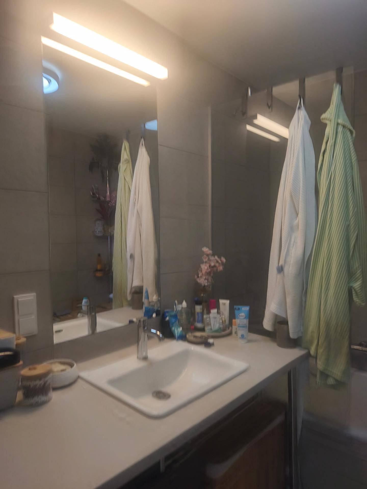 Modernes Badezimmer mit Einzelwaschbecken, großem Spiegel und grauen Fliesen an den Wänden.