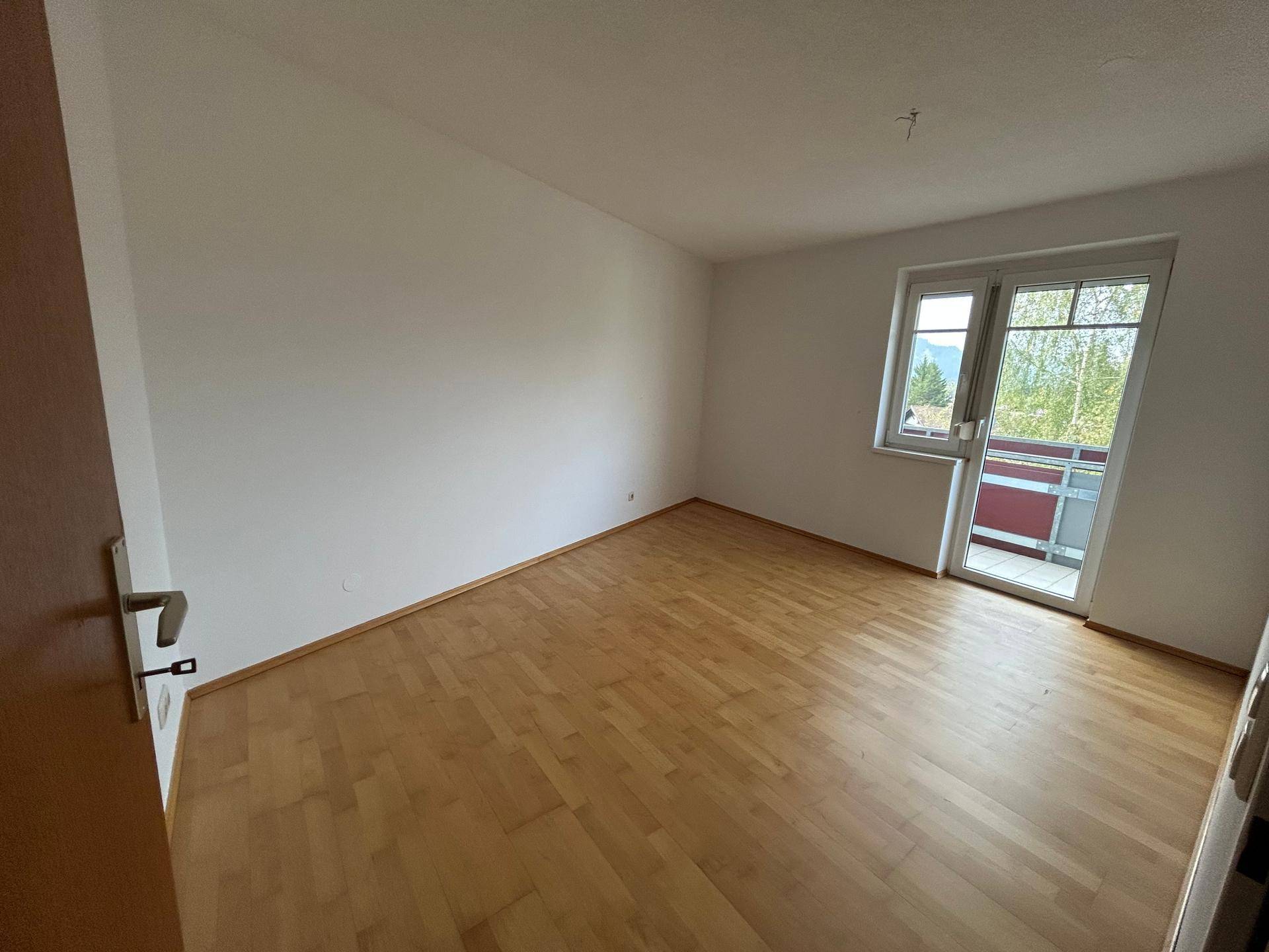 Helles Wohnzimmer mit Laminatboden und Balkonzugang, bietet viel Tageslicht.