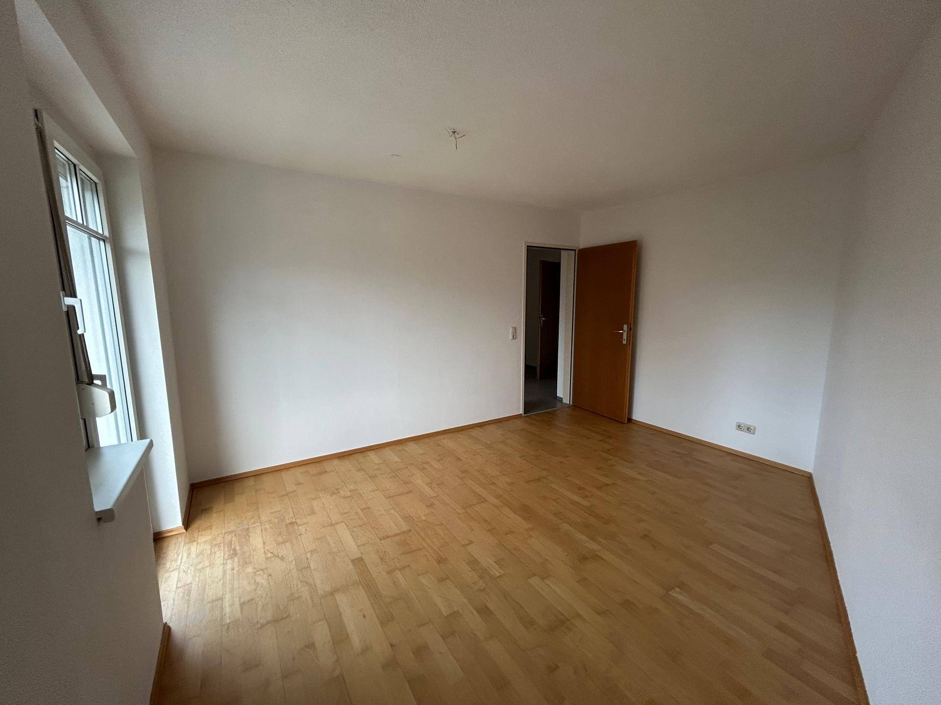 Helles Zimmer mit Laminatboden und einem Fenster, das viel natürliches Licht hereinlässt.