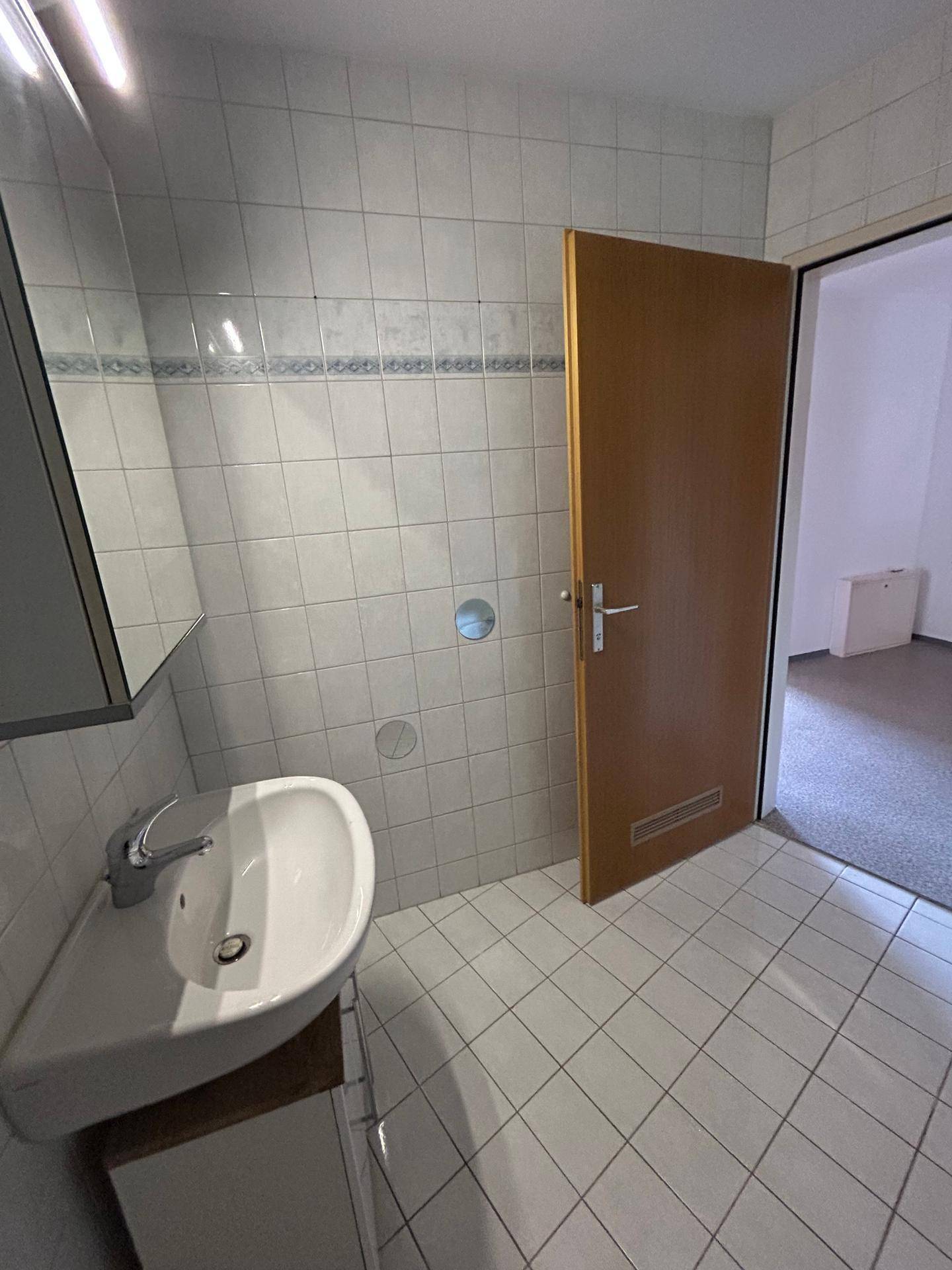 Kleines Badezimmer mit Waschbecken, Spiegelschrank und hellen Wandfliesen.