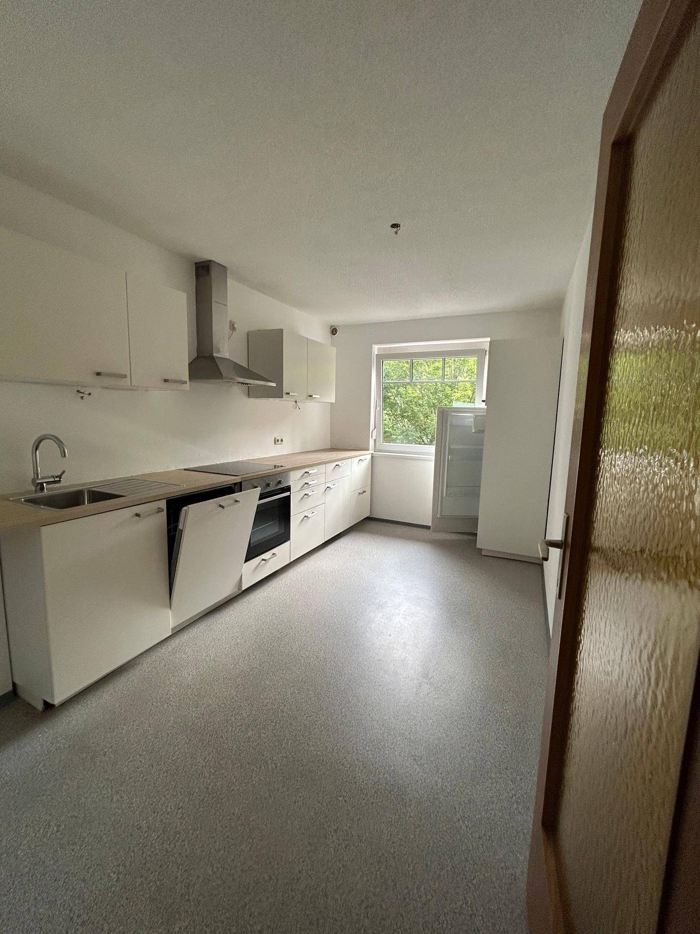 Funktionale Küche mit weißen Schränken, Holz-Arbeitsplatte und Fenster mit Blick ins Grüne.