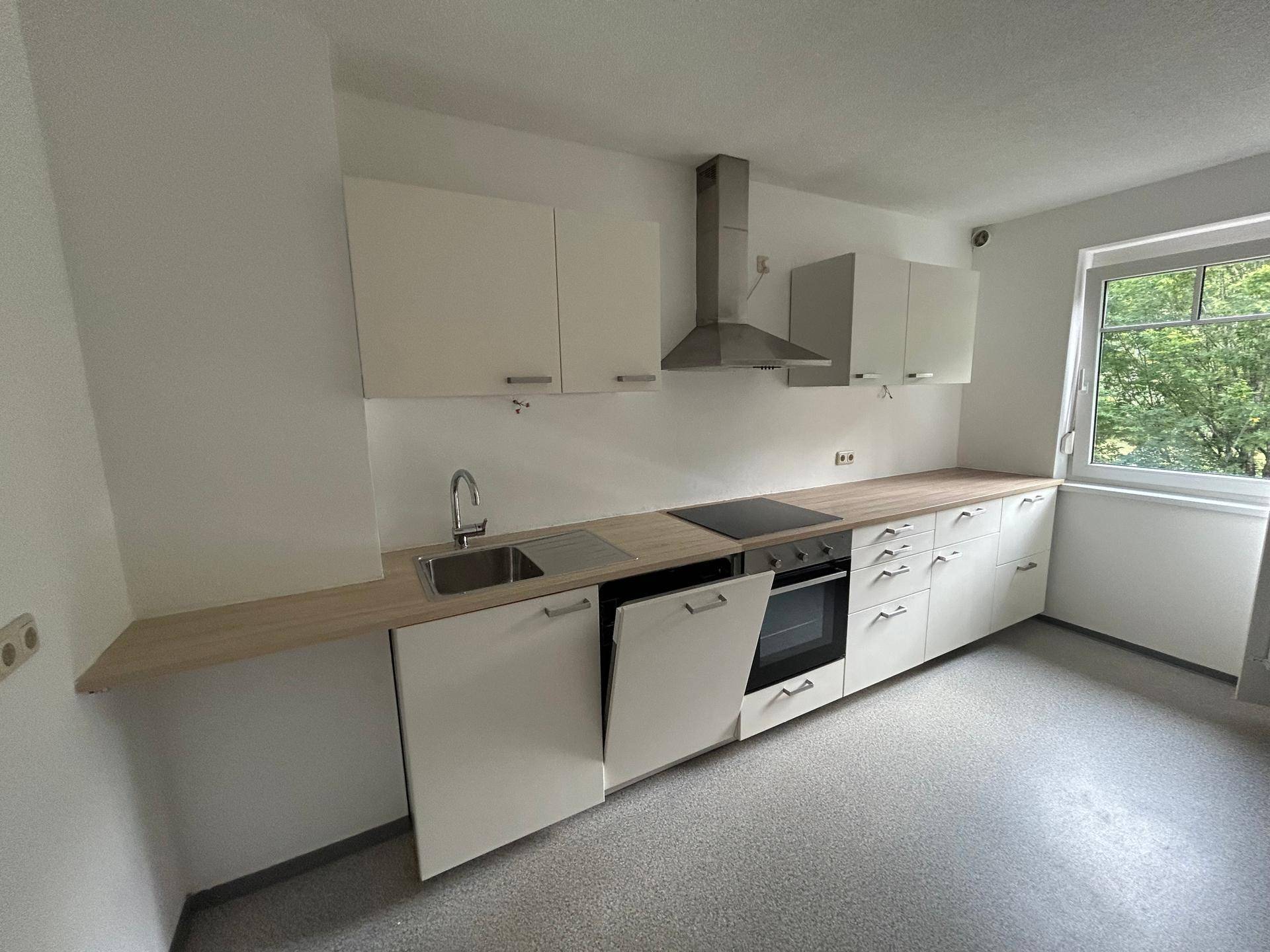 Moderne Einbauküche mit weißen Fronten, Holz-Arbeitsplatte und integrierten Geräten.