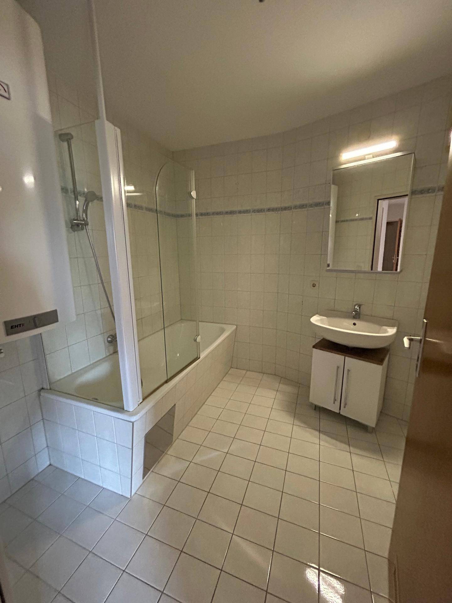 Badezimmer mit Badewanne, Duschabtrennung, Waschbecken und Wandfliesen in hellem Design.
