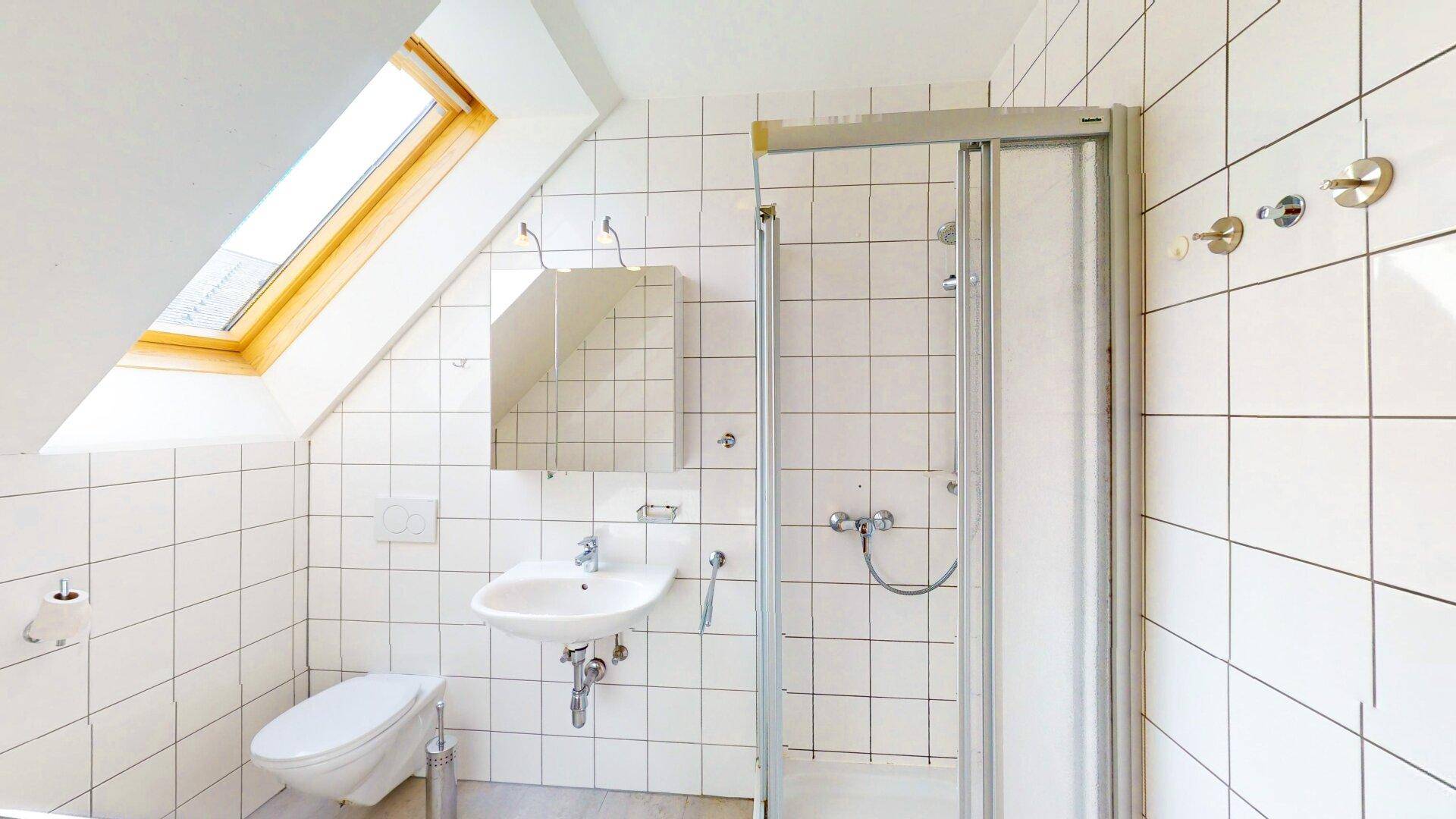 Helles Badezimmer mit weißen Fliesen, Dusche und Dachfenster in der Schräge.