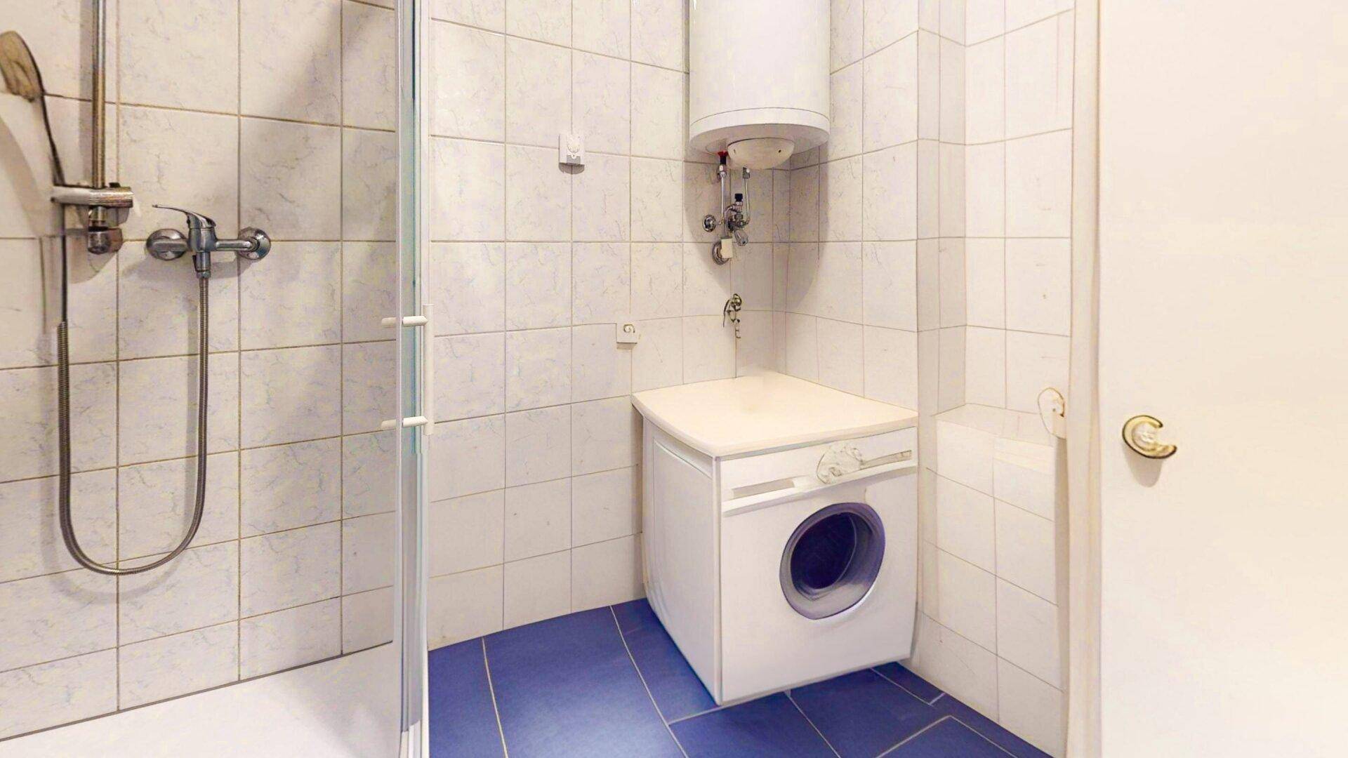 Badezimmer mit Duschkabine, Waschmaschine und Warmwasserboiler, praktisch eingerichtet.