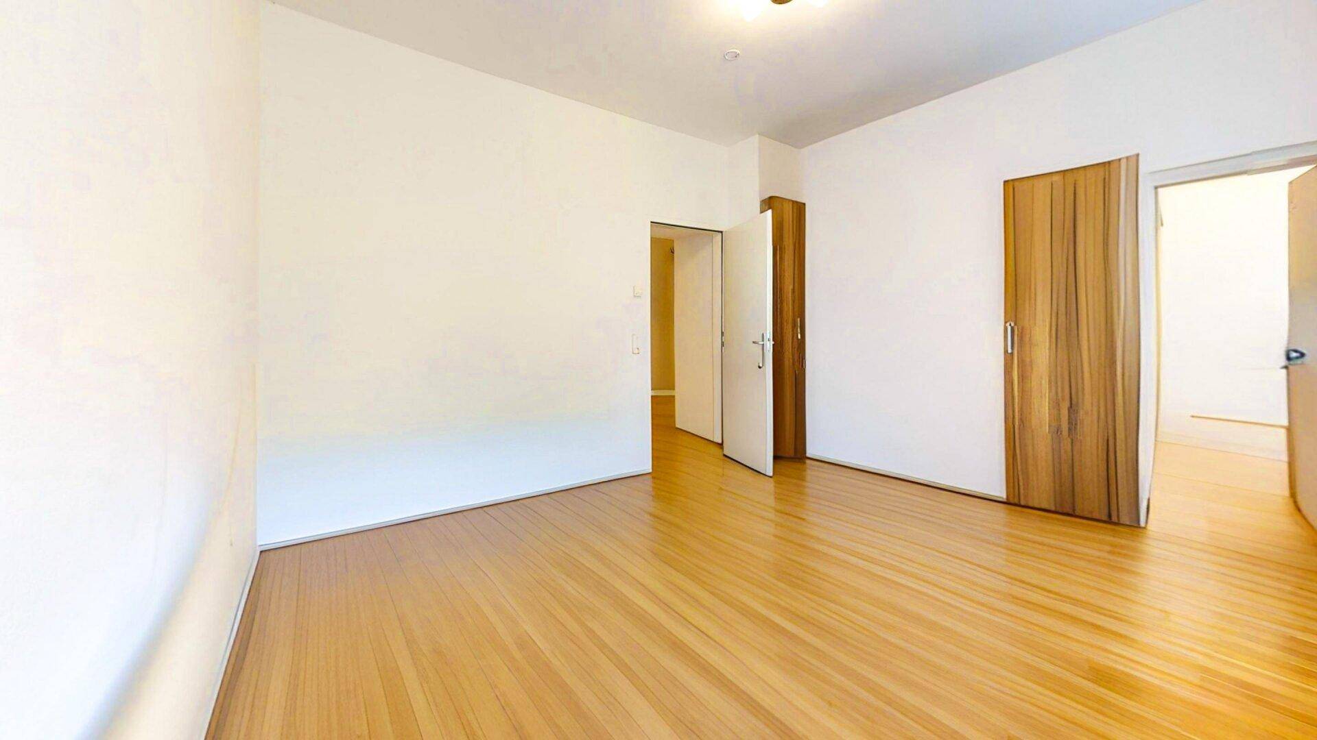 Geräumiges, leeres Zimmer mit hellem Holzparkett und weißen Wänden, ideal für Schlaf- oder Arbeitsbereich.